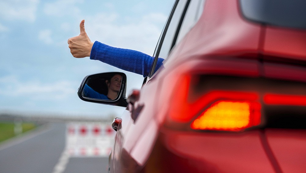 Der Fahrer eines roten Autos streckt seinen Arm aus dem Fenster und zeigt den „Daumen hoch“. 