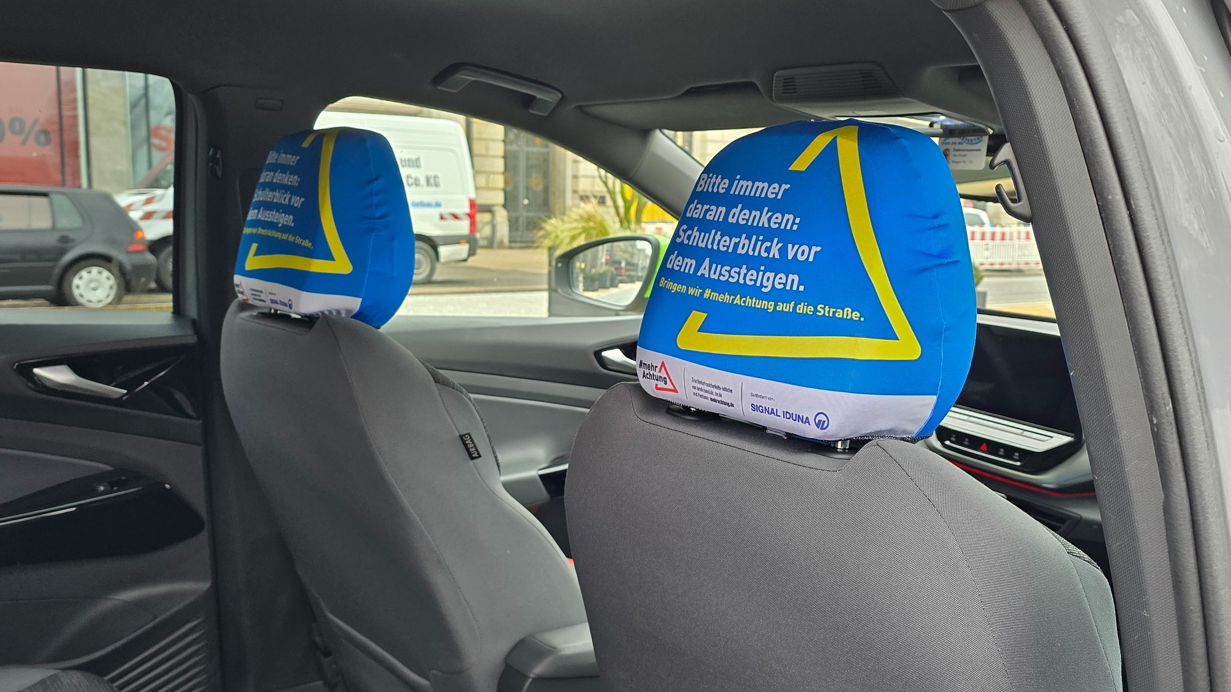 Die Kopfstützen eines Taxis tragen einen Bezug. Auf den Bezügen steht: Bitte immer daran denken: Schulterblick vor dem Aussteigen.