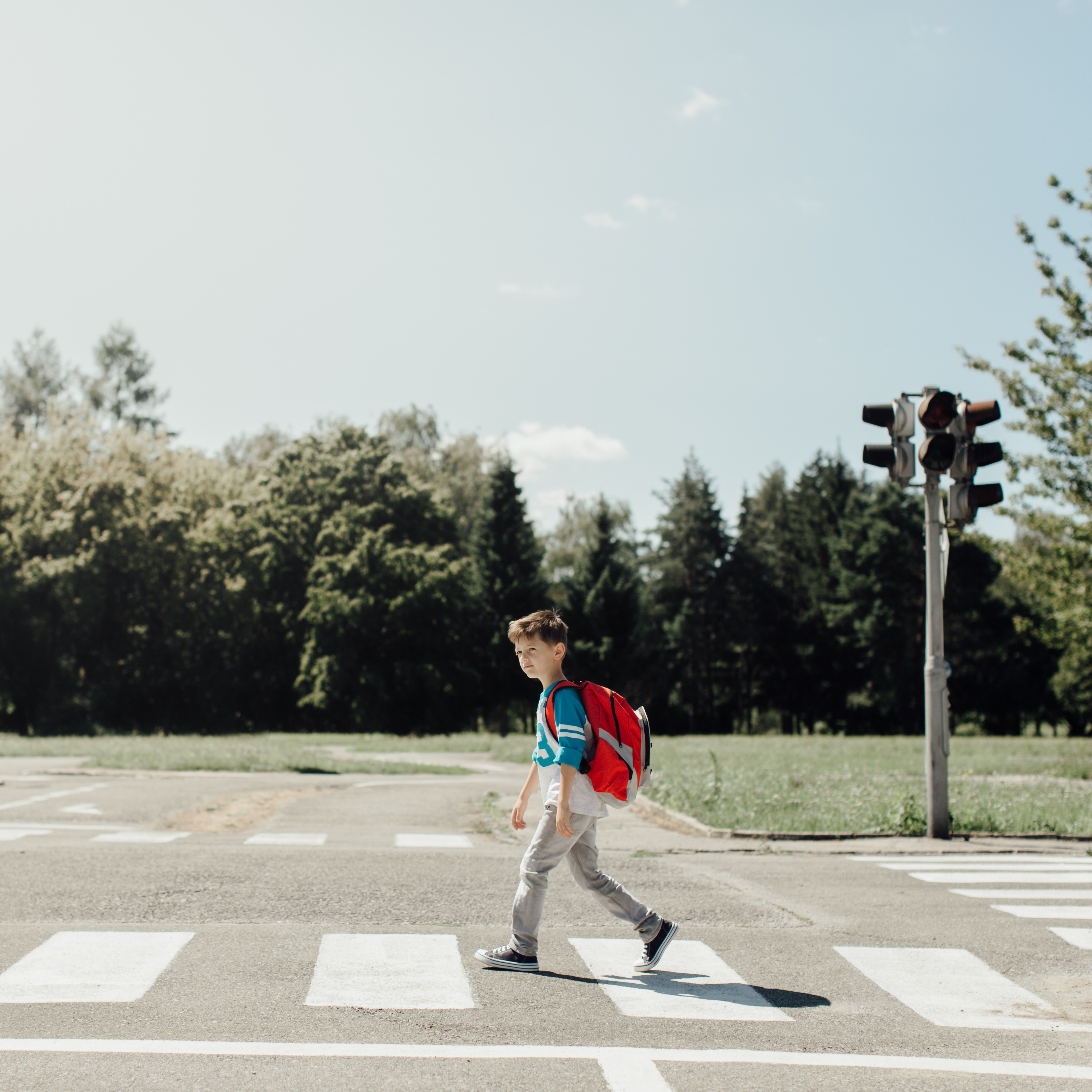 Ein Schuljunge mit einem roten Rucksack überquert eine Straße auf einem Zebrastreifen.  