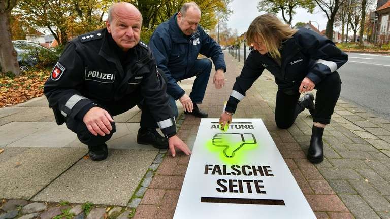 falsche-seite Drei Polizisten hocken neben und auf einem Radweg. Eine Polizistin hat dabei eine Sprühdose mit gelber Farbe in der Hand und besprüht eine Schablone. Die Schablone weist darauf hin, dass aus dieser Fahrtrichtung kommende Radfahrende auf der falschen Seite
des Radwegs unterwegs sind.