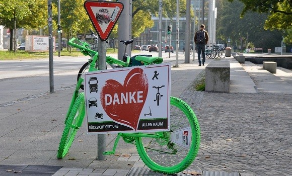 Ein knallgrün angesprühtes Fahrrad mit einem großen Schild steht an einem
Laternenpfahl.