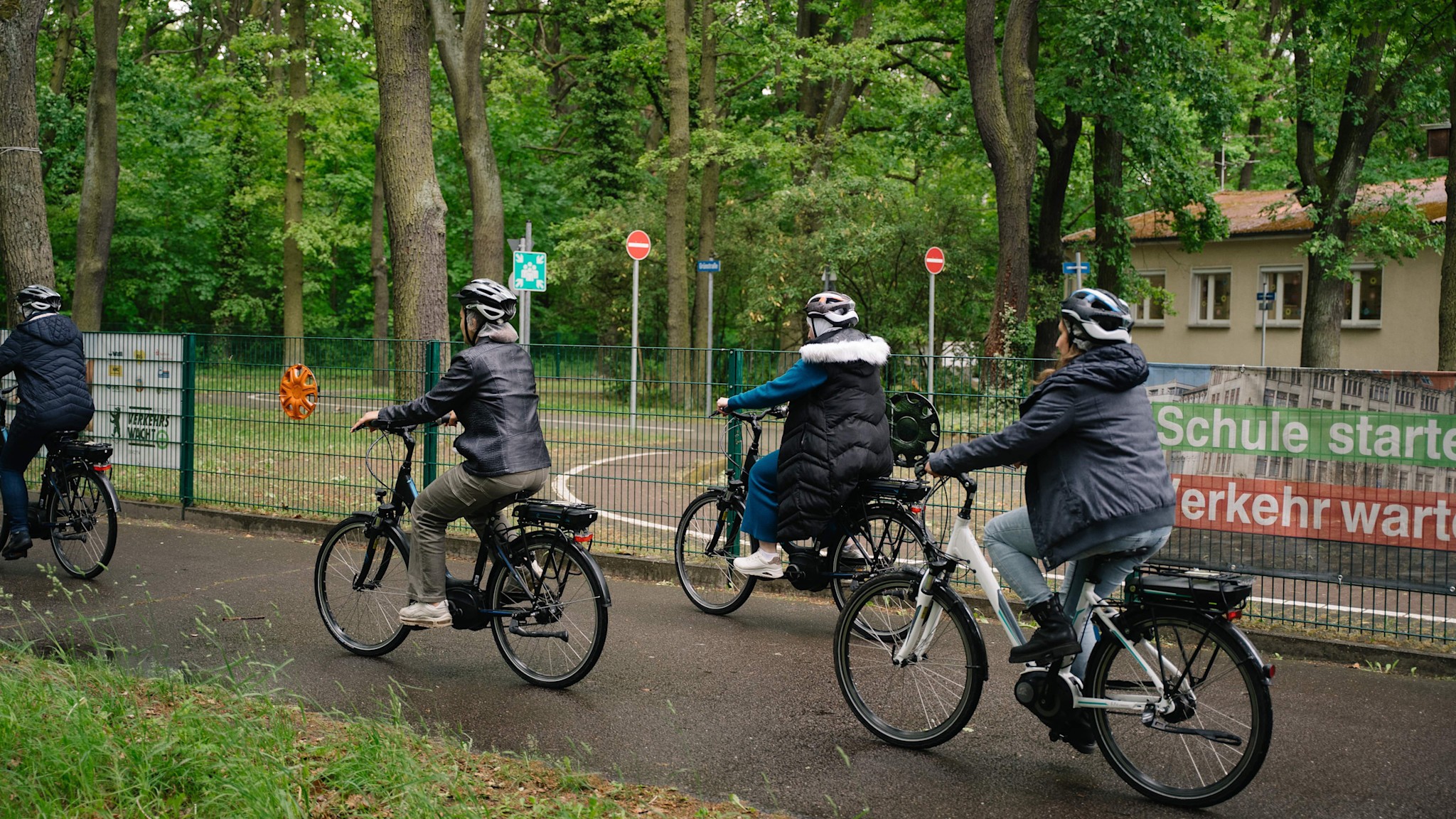 Vier Personen fahren mit Pedelecs auf einem asphaltierten Weg im Volkspark Wuhlheide in Berlin.