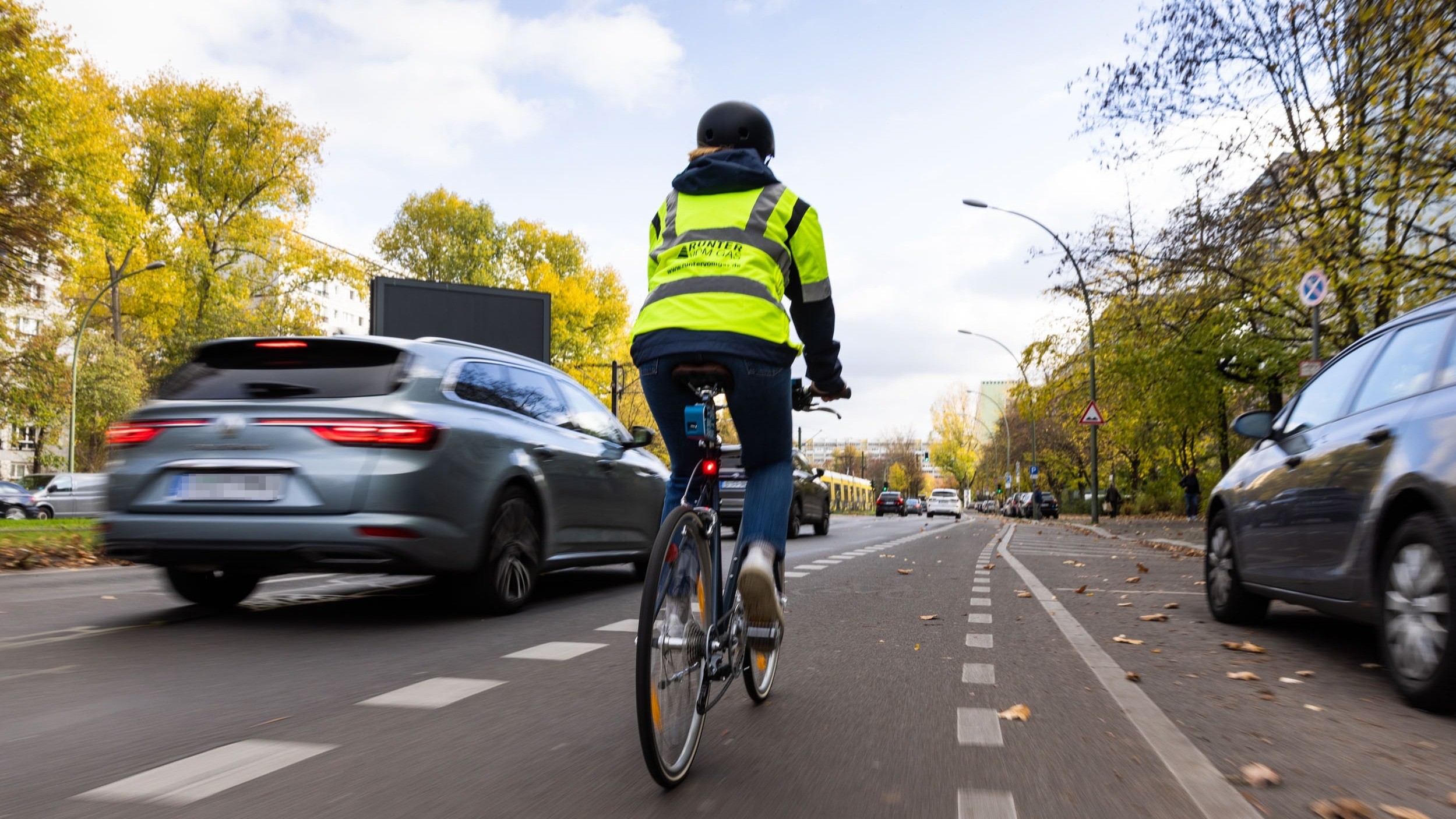 Eine Frau fährt mit ihrem Fahrrad auf dem Radweg neben einem Pkw im Stadtverkehr. 