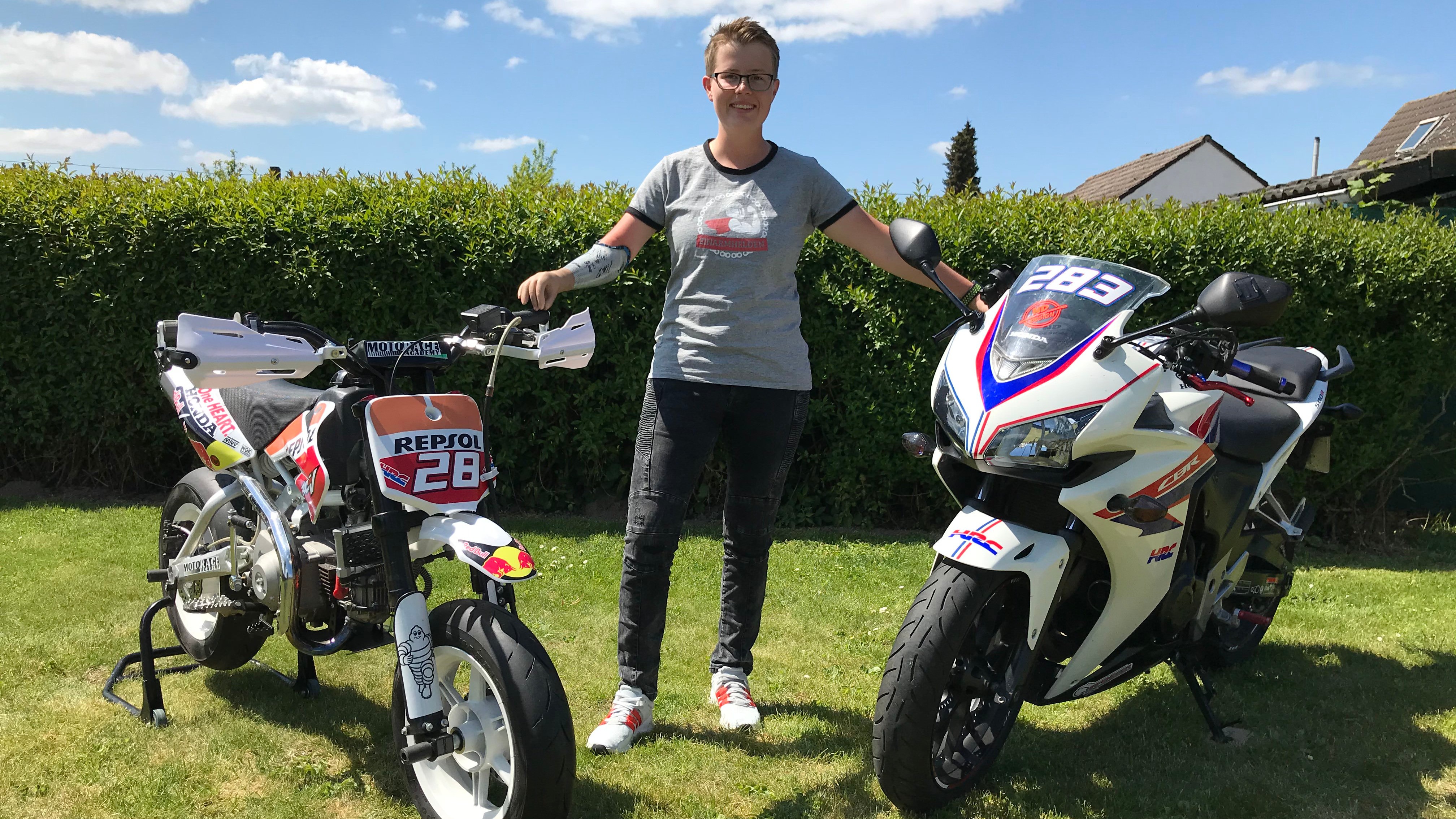 Header Motorrad fahren mit Behinderung Jolene Lack (16:9) Jolene Lack auf einer Wiese, links und rechts von ihr sind ihre beiden Motorräder zu sehen.