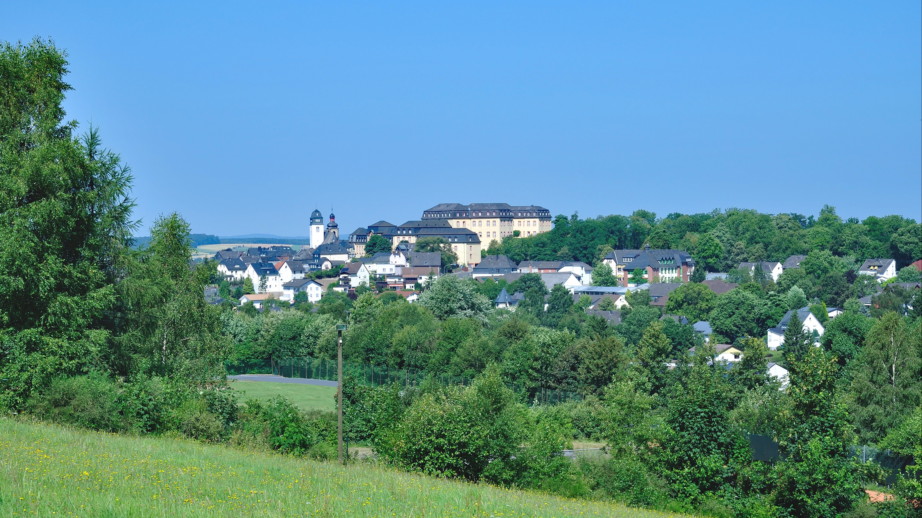 Jugendtaxi: Header Dorflandschaft 16:9 Das Bild zeigt ein Dorf inmitten einer grünen Landschaft.