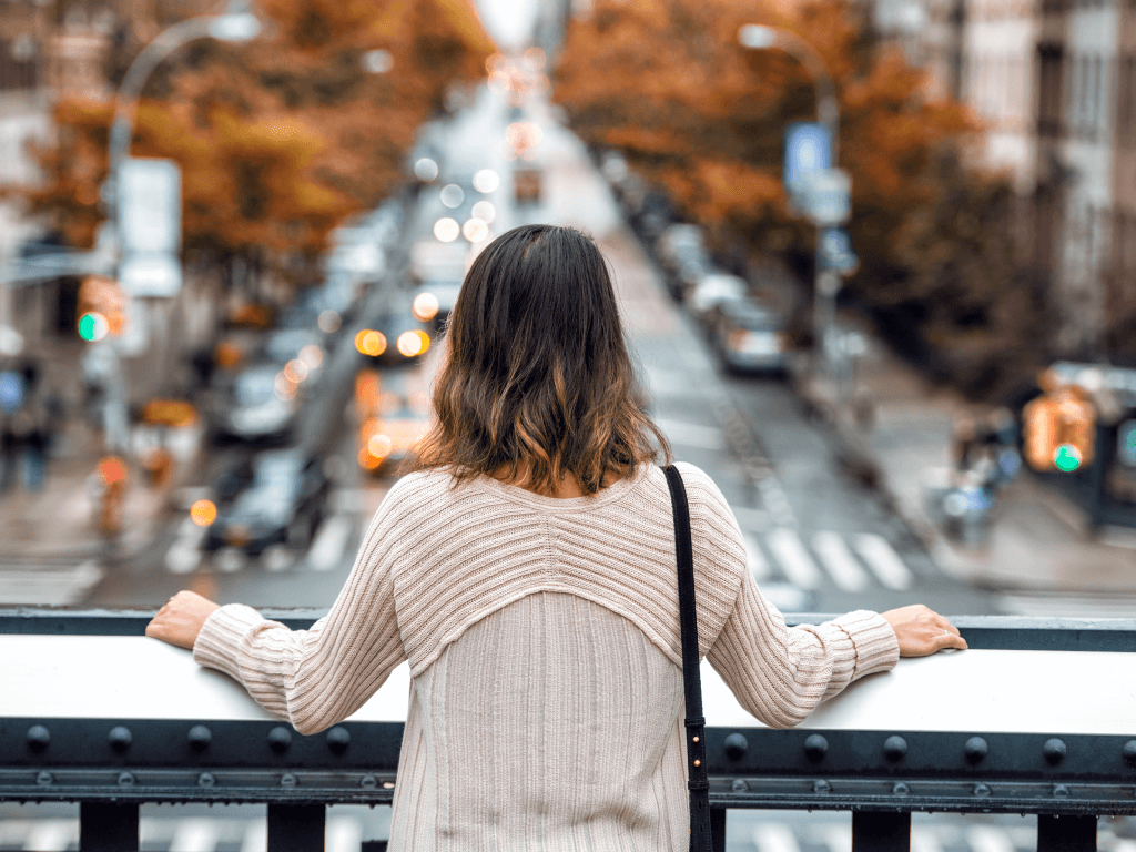 Eine Frau sieht von einer Brücke herab auf den Straßenverkehr. Sie wirkt dabei gelassen.