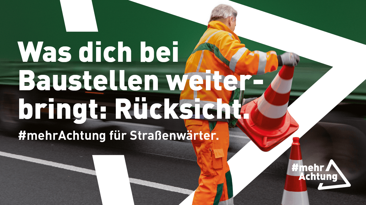 Ein Straßenwärter in Warnkleidung sichert eine Baustelle auf einer Straße mit einem rot-weißen Leitkegel ab, während im Hintergrund der Verkehr vorbeifährt. 