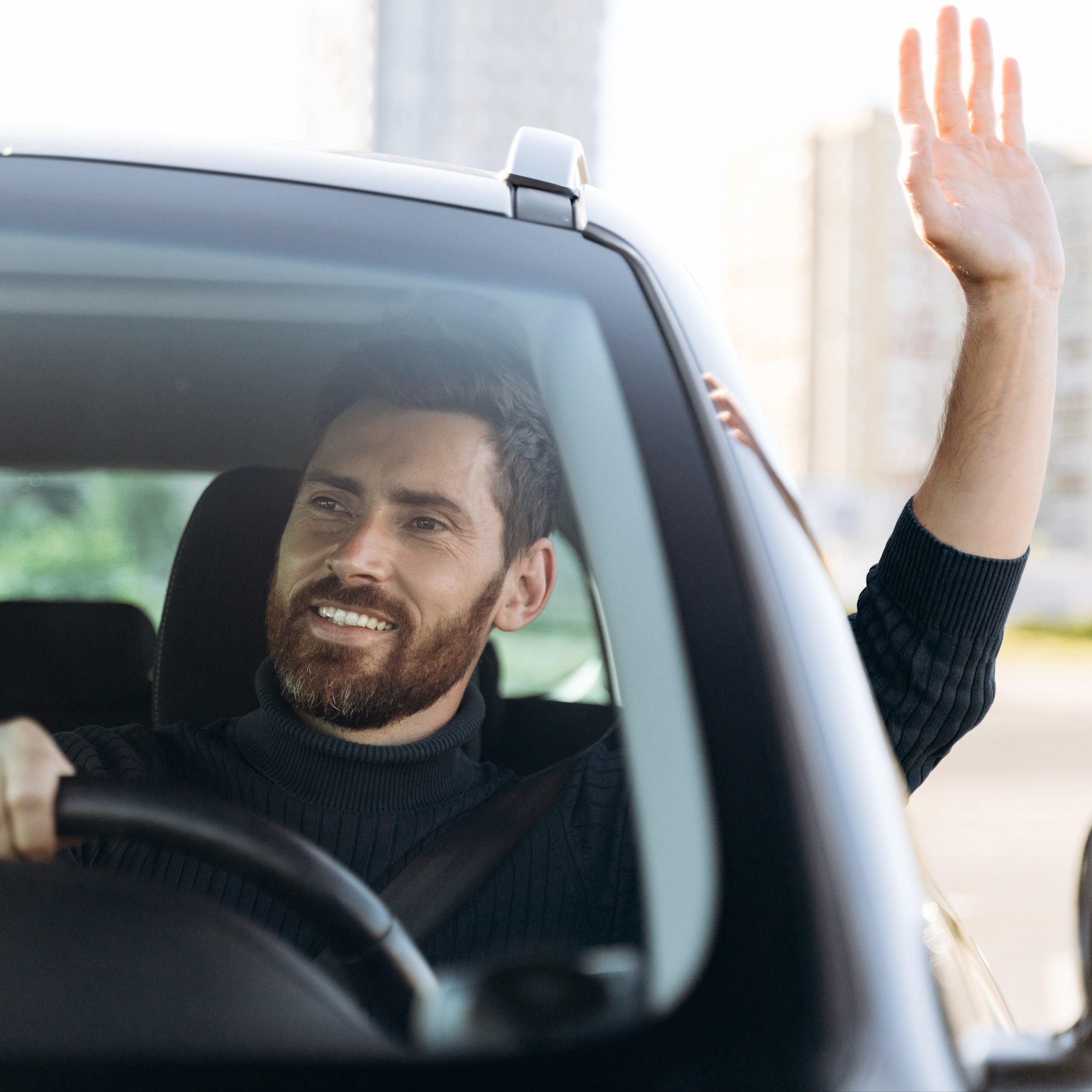 Auto vs Fahrrad – Mann im Auto Ein Autofahrer winkt aus dem Fenster eines Autos und guckt freundlich.