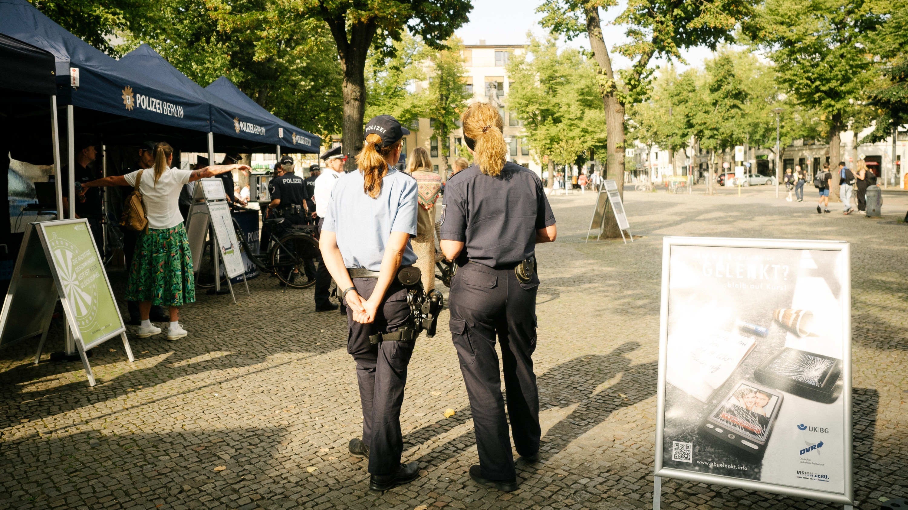 Zwei Polizistinnen in Uniform blicken auf den Marktplatz Friedrichshagen. Im Hintergrund sind Aktionsstände mit der Aufschrift „Polizei Berlin“ zu sehen.