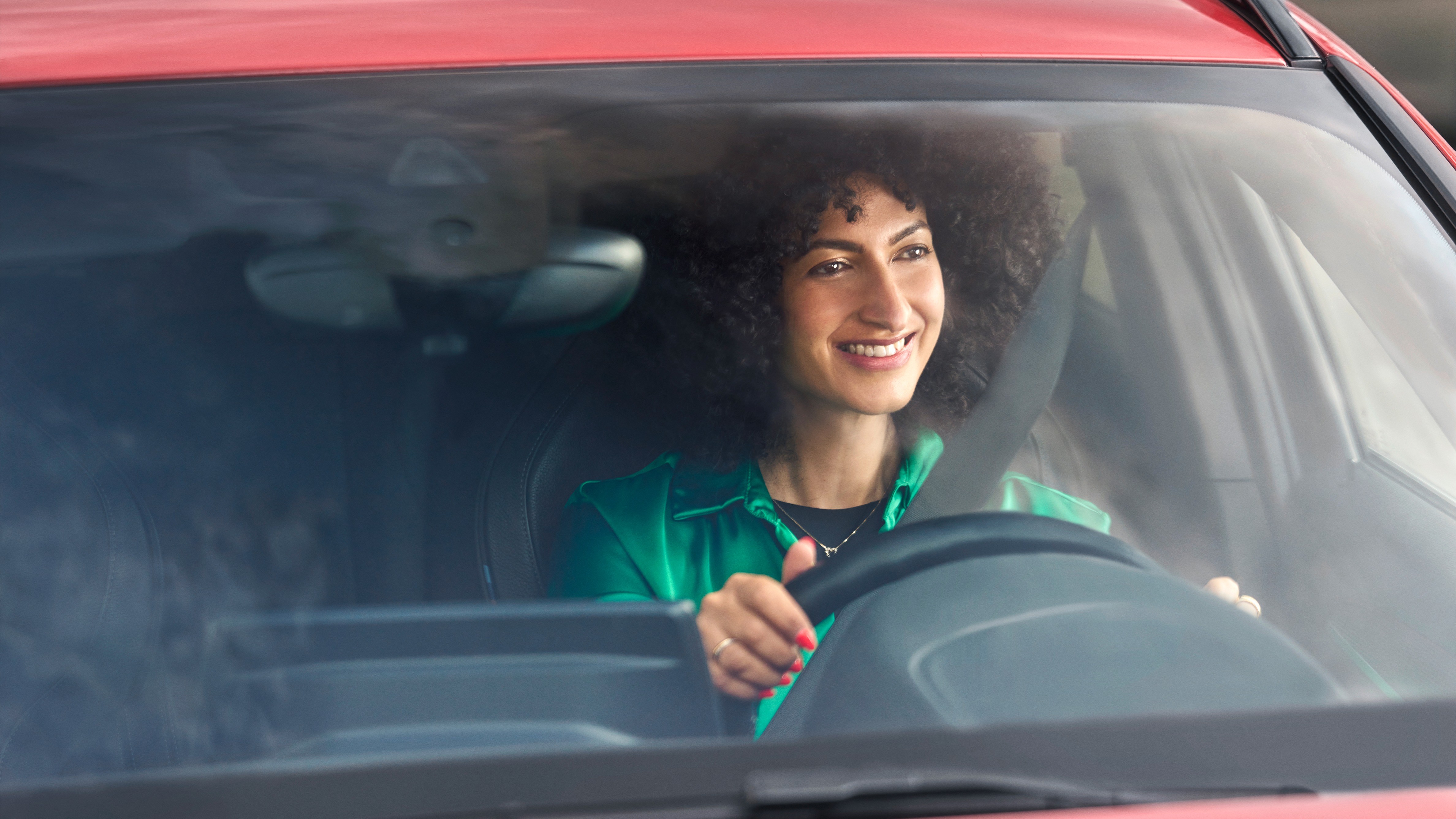 Eine Frau sitzt am Steuer eines Autos und lächelt. 