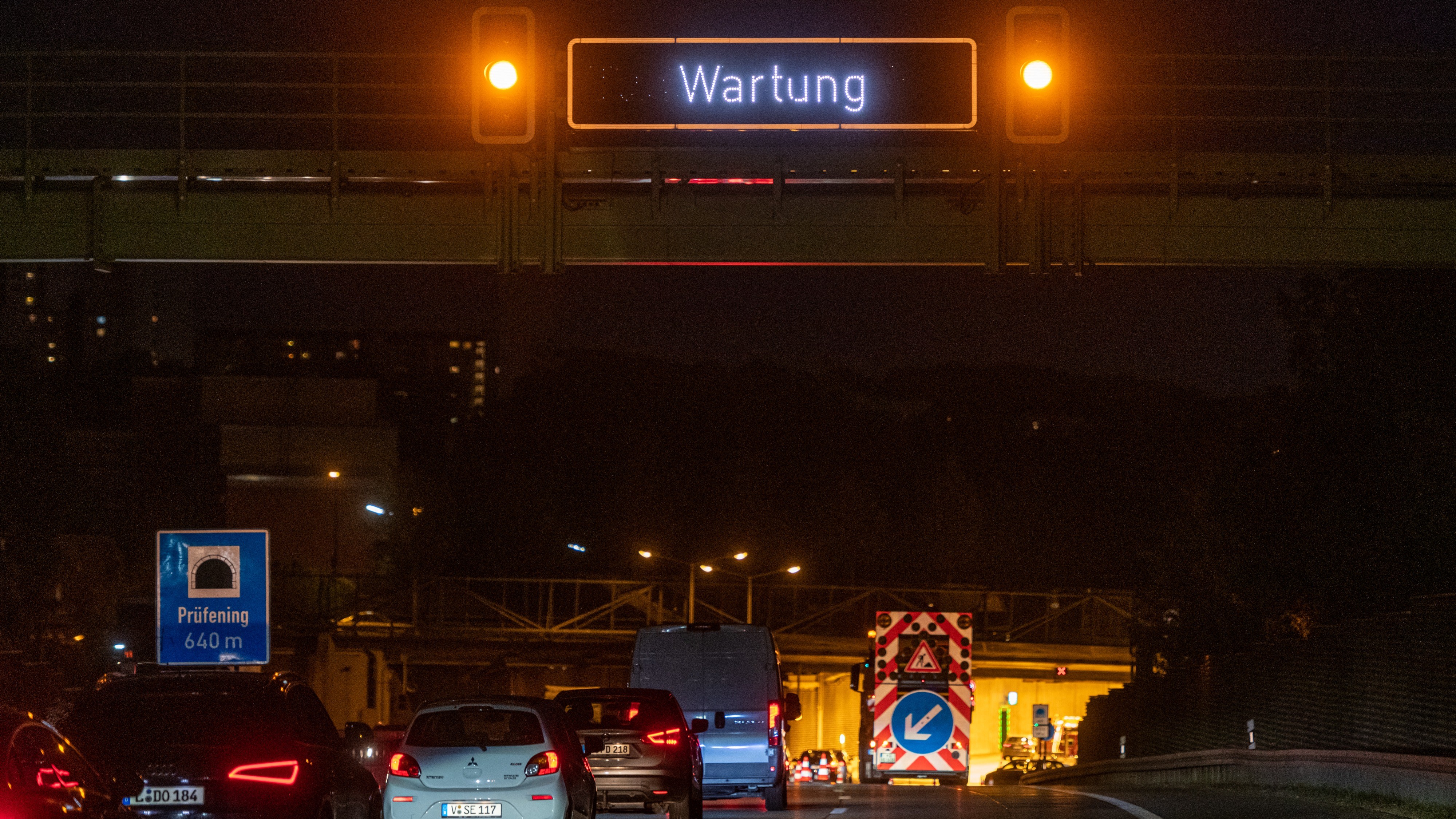 Das Bild zeigt eine Tunneleinfahrt. Die rechte Spur ist durch ein Fahrzeug der Autobahnmeisterei gesperrt. Ein digitales Autobahnschild zeigt den Hinweis „Wartung“. 