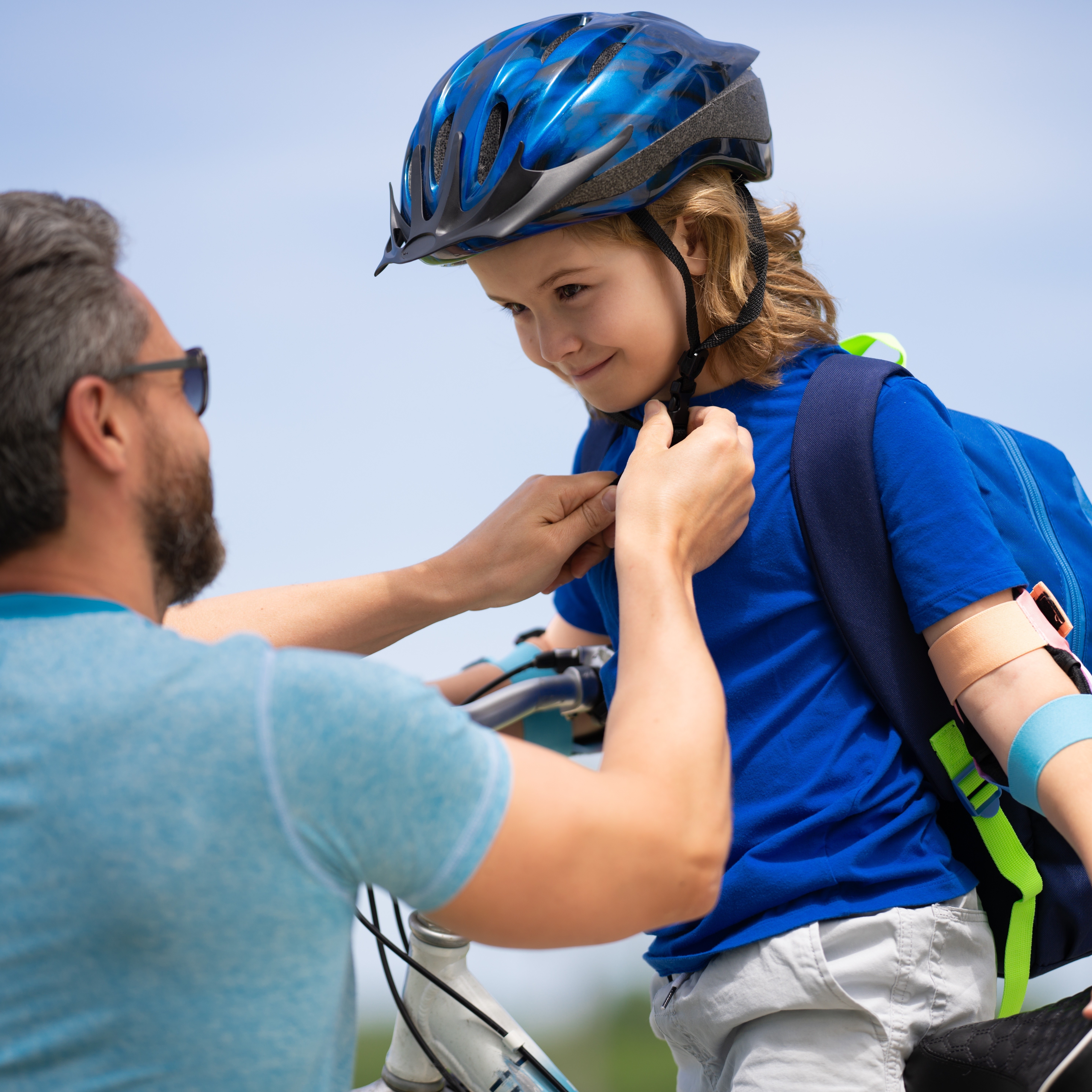 Radfahrausbildung – Kind mit Helm Ein Vater schließt den blauen Fahrradhelm seines Sohnes.