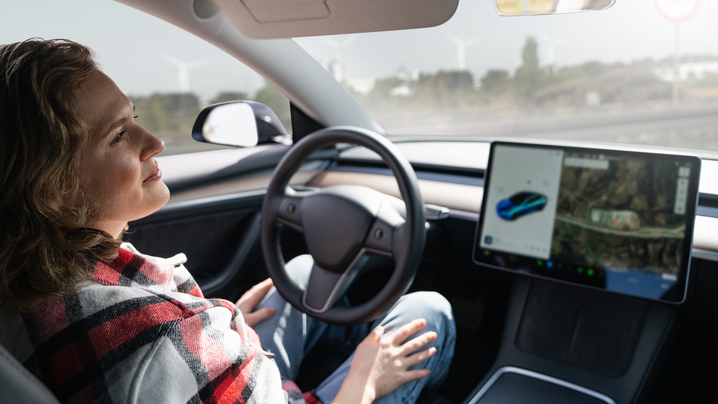 Header Autonomes Fahren Eine Frau sitzt am Steuer eines Fahrzeuges und wendet den Blick ab. Ihre Hände sind nicht am Steuer.