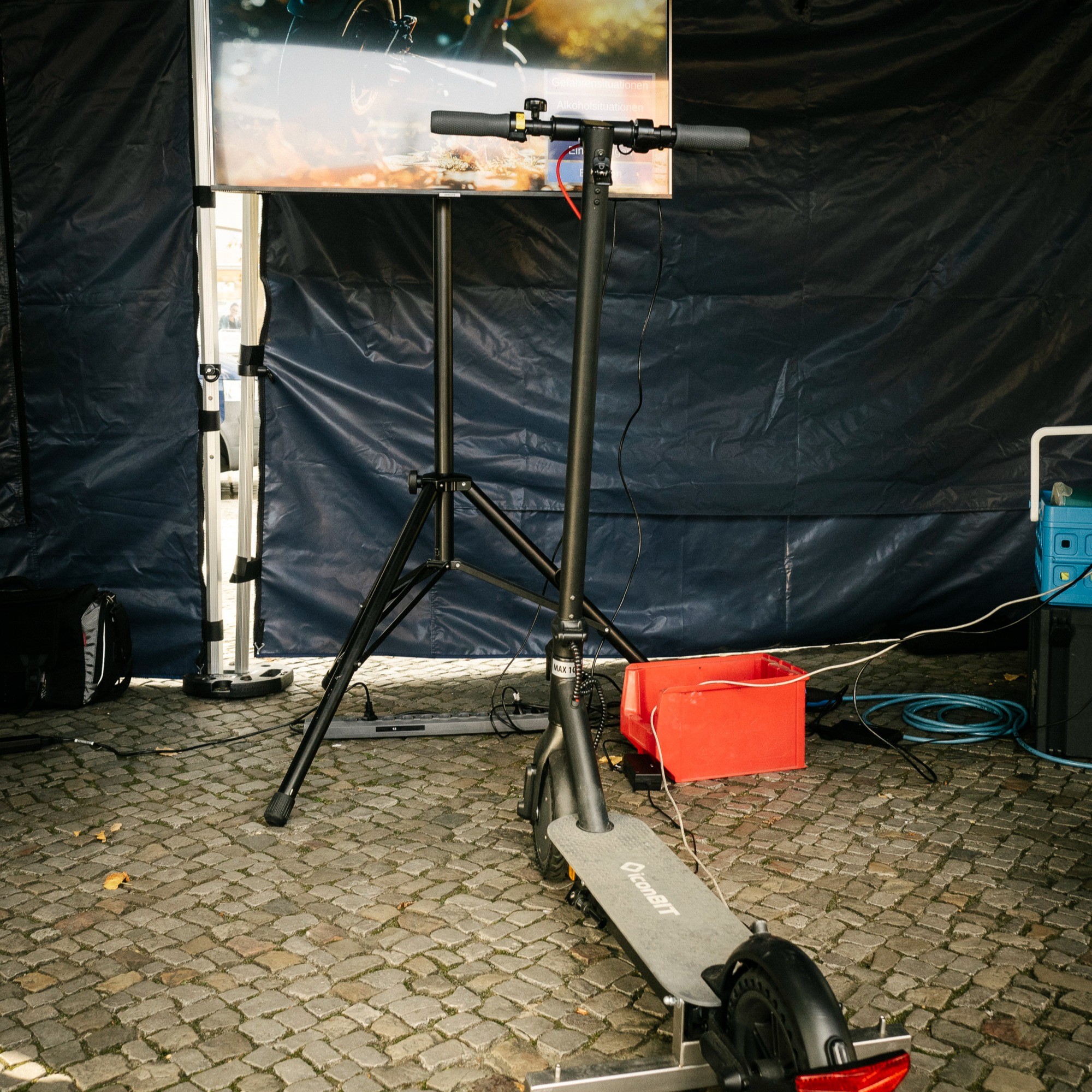 Das Bild zeigt einen Elektroscooter, der an einen Bildschirm angeschlossen ist. Es ist der E-Scooter-Simulator der Polizei Berlin.