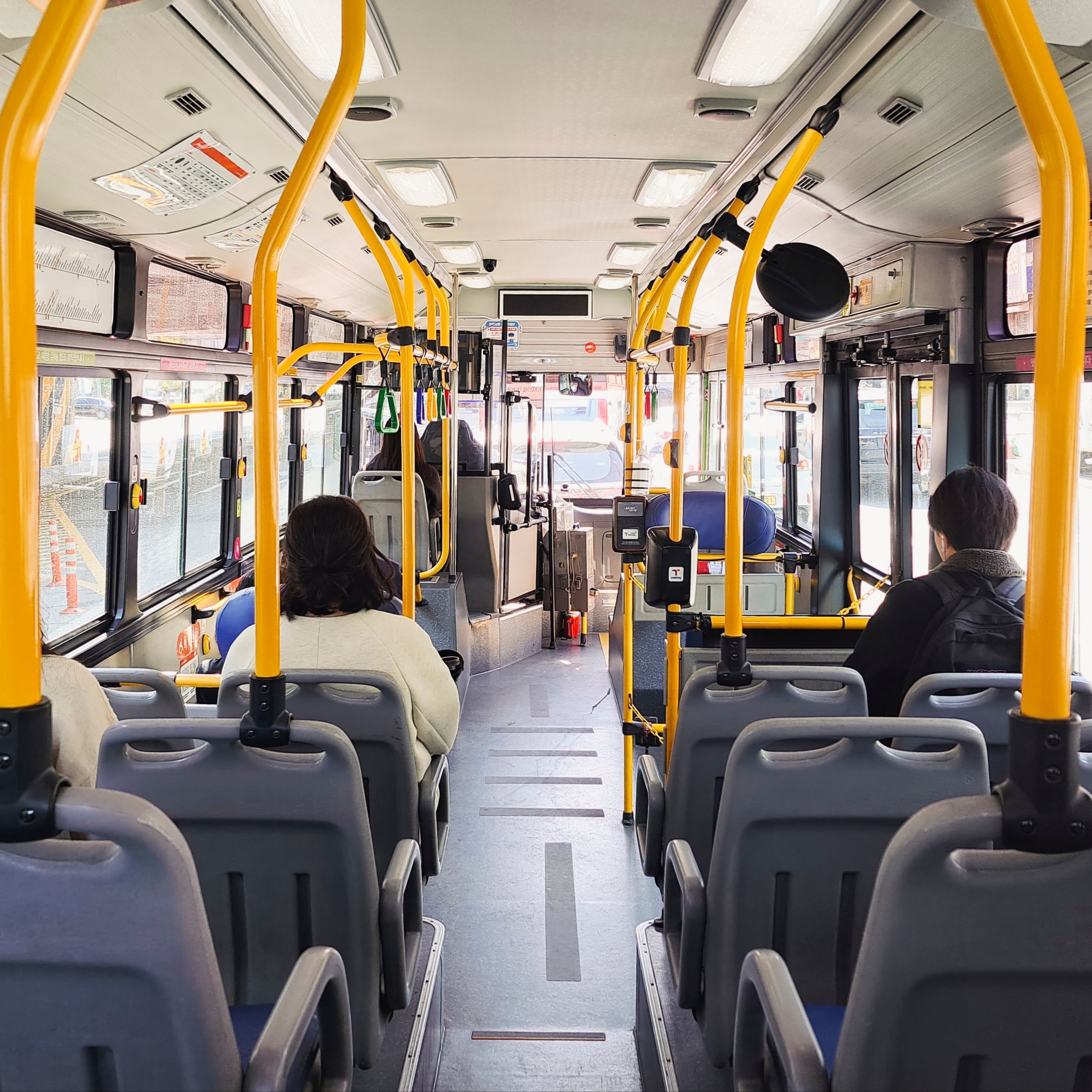 Der helle Innenraum eines modernen Linienbusses mit wenigen Fahrgästen. Der Blick geht durch den Mittelgang nach vorne.