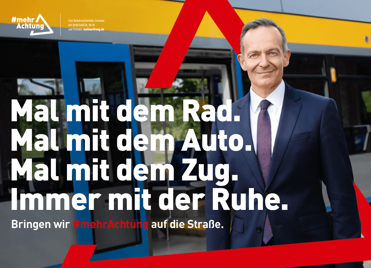 Das Motiv zeigt Bundesverkehrsminister Dr. Volker Wissing im Anzug vor einer Tram. In einem roten Dreieck, das grafisch über das Bild gelegt ist und an das Verkehrszeichen „Gefahrenstelle“ erinnert, steht der Text: „Mal mit dem Rad. Mal mit dem Auto. Mal mit dem Zug. Immer mit der Ruhe. Bringen wir #mehrAchtung auf die Straße.“