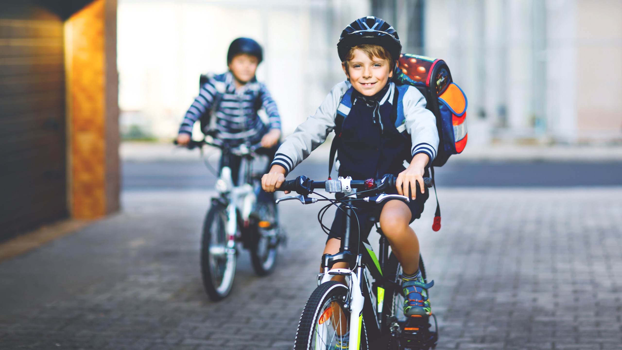 7 Tipps Schulweg Fahrrad Jungs Zwei Grundschulkinder mit Helmen und Schulranzen fahren mit dem Fahrrad sicher zur Schule.