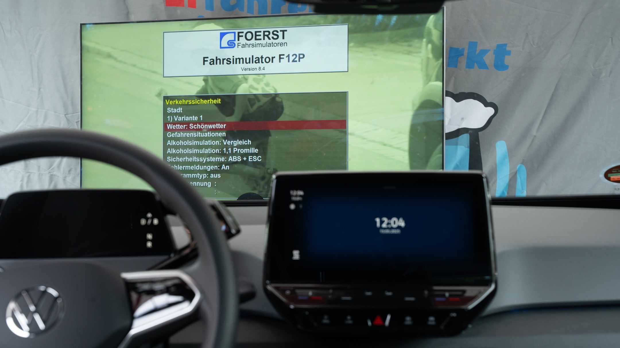 Blick ins Cockpit eines Auto-Fahrsimulators: Lenkrad, Display und Bildschirm mit Benutzeroberfläche. Die Simulation zeigt 1,1 Promille Alkohol und verschiedene Fahrszenarien wie Schönwetter. Das System „FOERST F12P“ visualisiert alkoholbedingte Einschränkungen im Straßenverkehr.