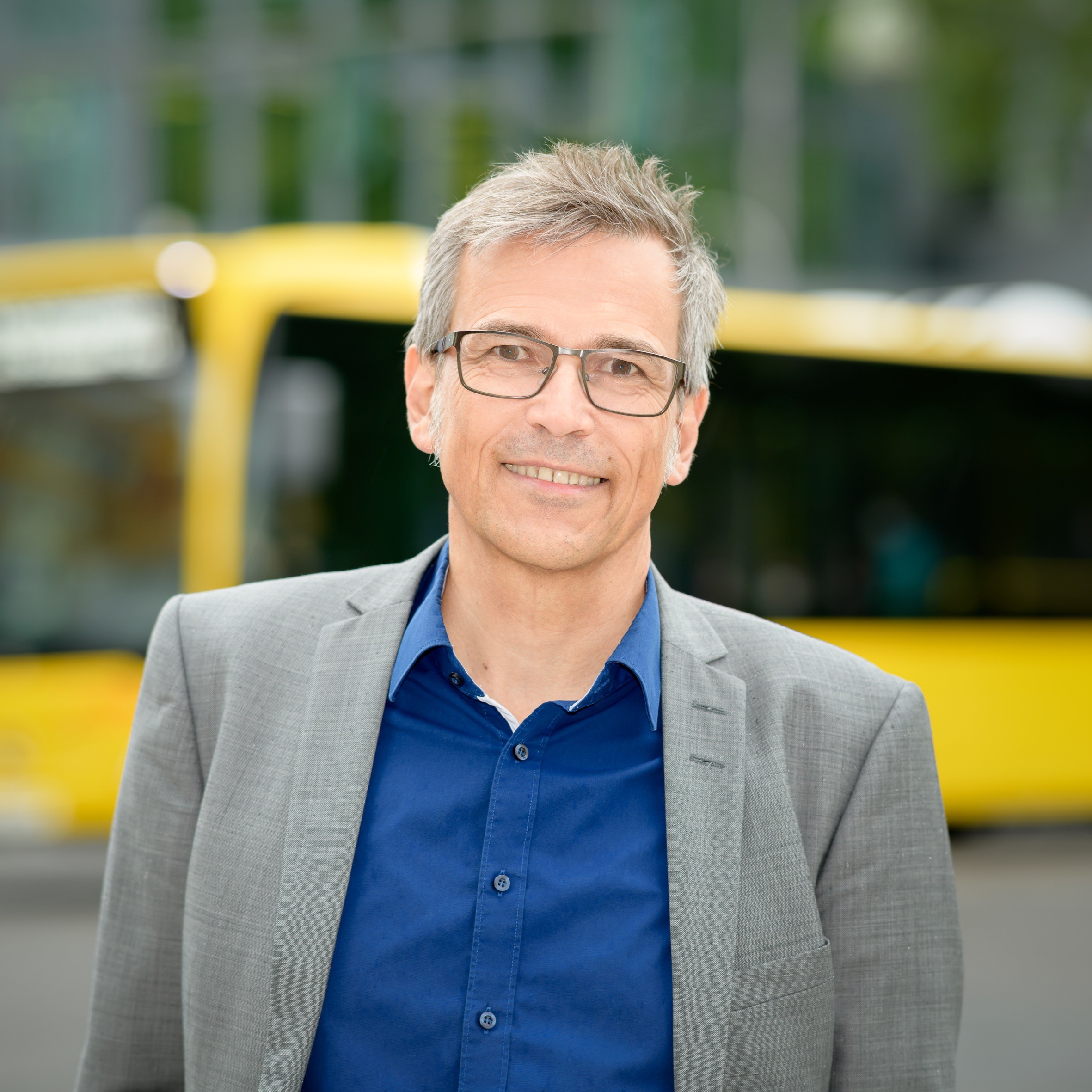 Radfahrausbildung_Josef Weiß Ein Mann im grauen Anzug steht vor einem gelben Bus und lächelt. Es ist Josef Weiß.