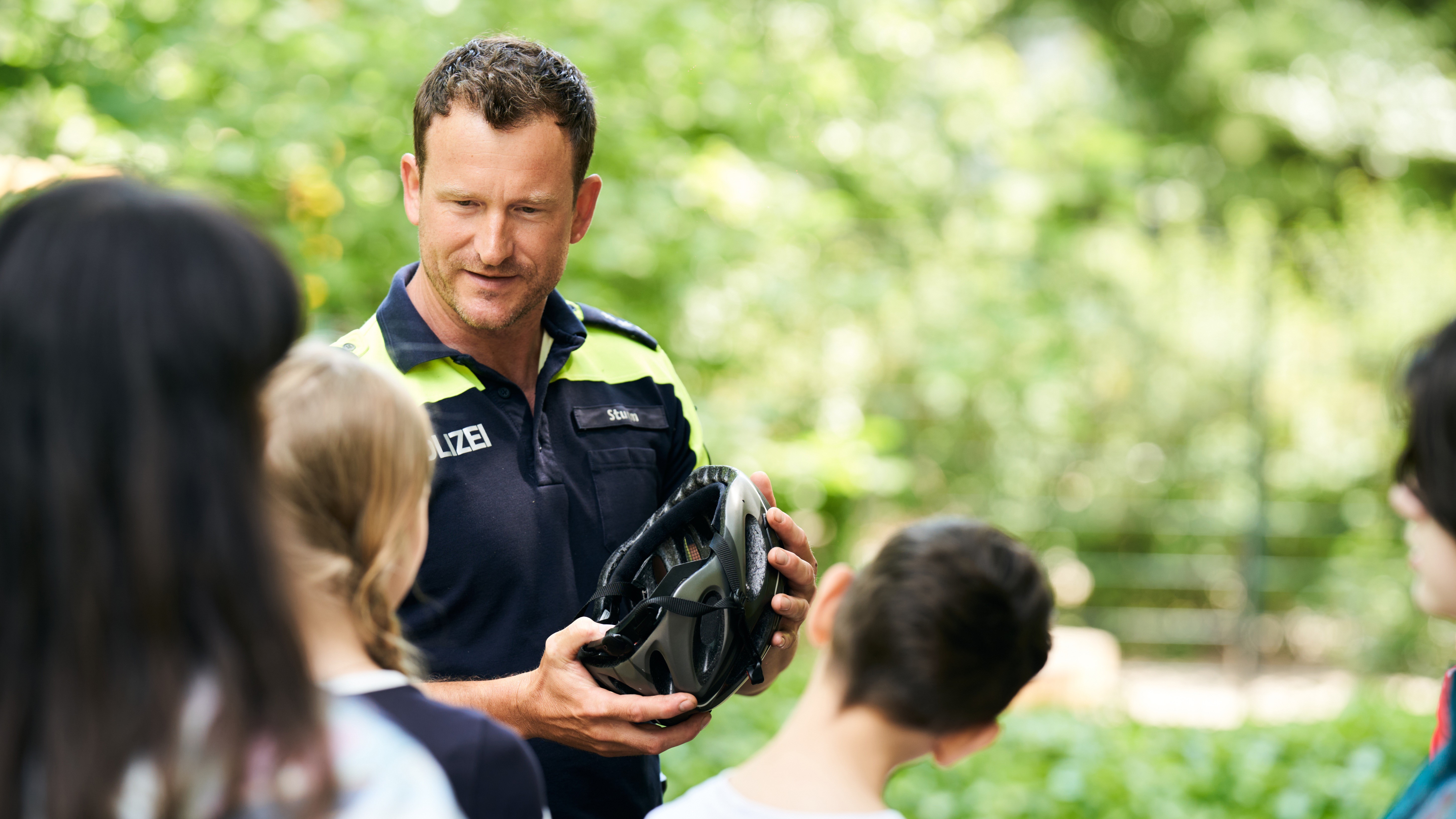 Ein Polizist spricht mit einer Gruppe von Schülerinnen und Schülern, wie wichtig es ist, beim Fahrradfahren einen Helm zu tragen.