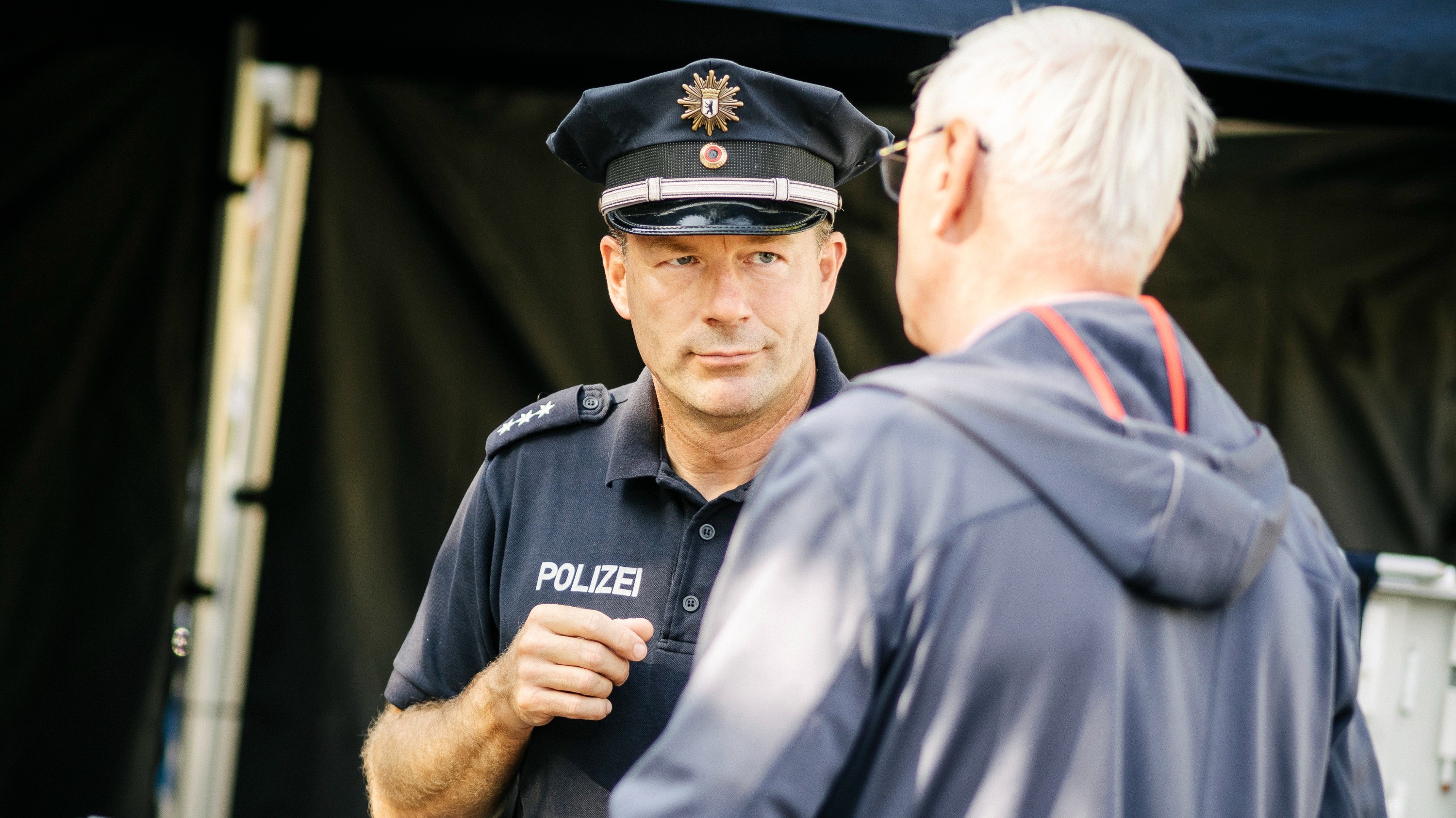 Ein älterer Herr mit weißem Haar unterhält sich mit einem Polizisten.