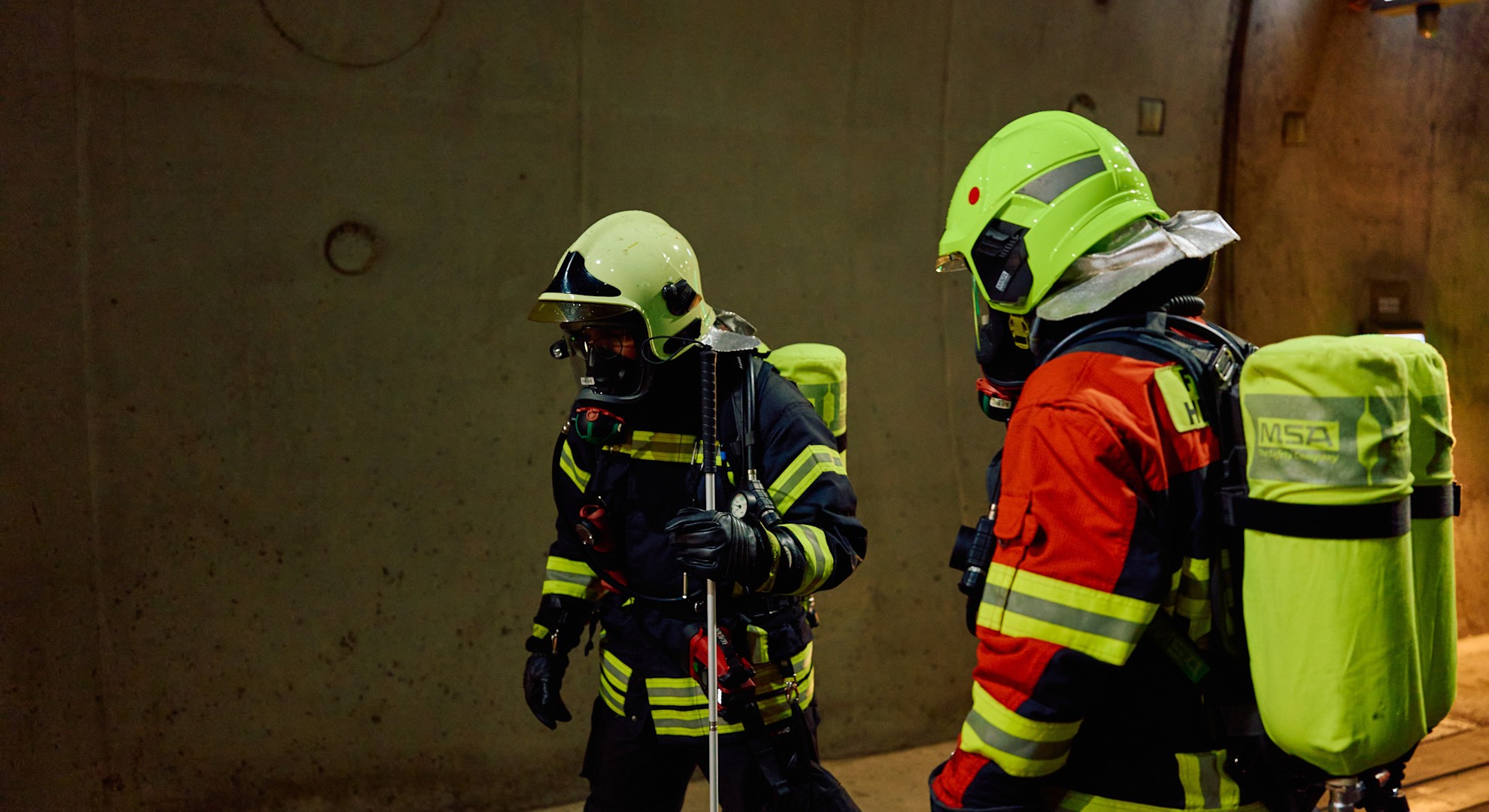 Volle Ausrüstung für den Ernstfall: Zwei Feuerwehrleute suchen im Tunnel nach Verletzten. Der Feuerwehrmann links nutzt einen speziellen Suchstock zur Orientierung. Dieser gehört zur tunnelspezifischen Sonderausrüstung.