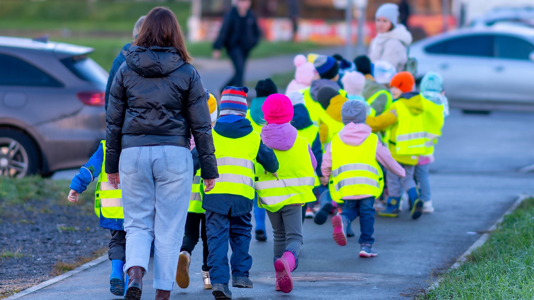 7 Tipps Schulweg Kinder in Warnwesten Schulwegsicherheit im Walking Bus: Eine Gruppe von Kindern in leuchtend gelben Warnwesten geht gemeinsam mit Erwachsenen sicher zur Schule.