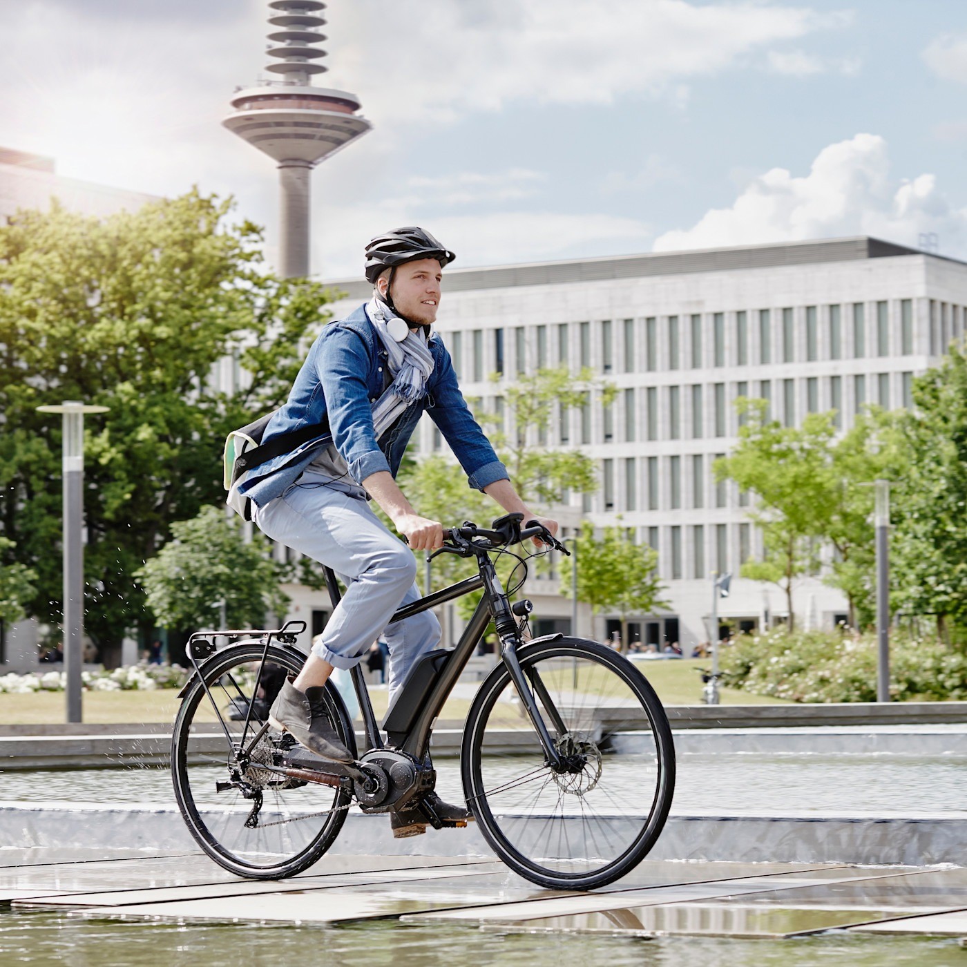 Mann mit Helm auf einem E-Bike Ein Mann mit Helm fährt auf einem E-Bike durch die Stadt. Im Hintergrund sind Bäume und Gebäude zu sehen.