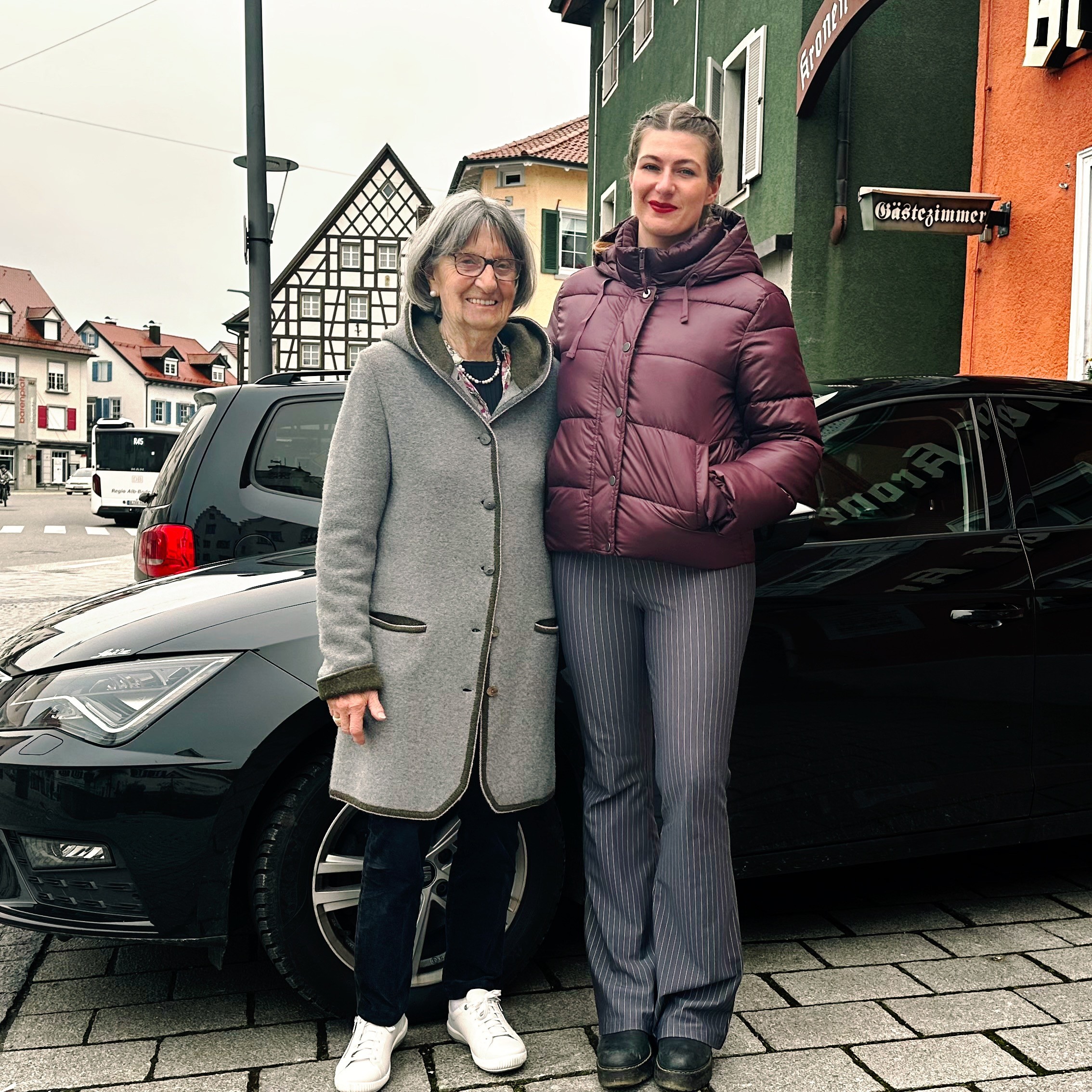 Header mit90nochmobil square Eine ältere und eine jüngere Frau stehen vor einem schwarzen Auto und lächeln in die Kamera.