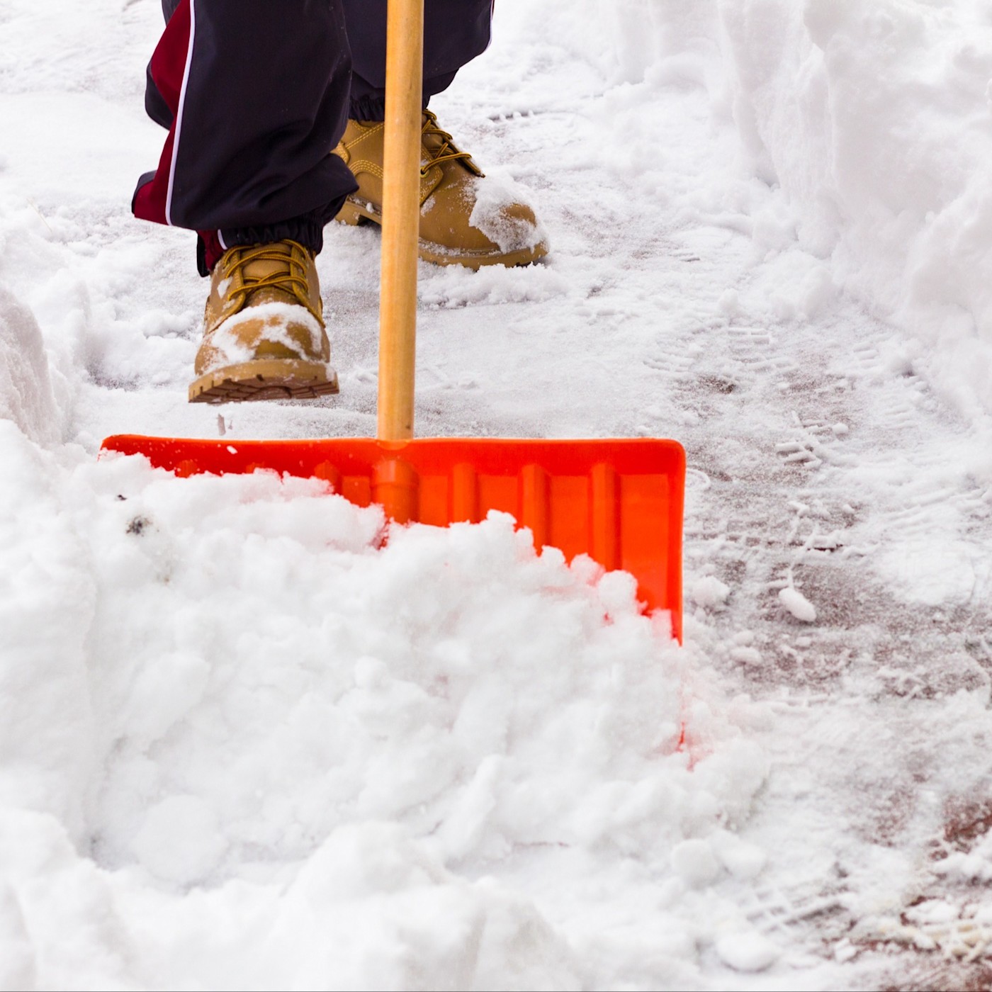Gehwege Schnee Das Bild zeigt einen verschneiten und vereisten Gehweg, der von einer Person mit einer Schneeschaufel freigeschoben wird.