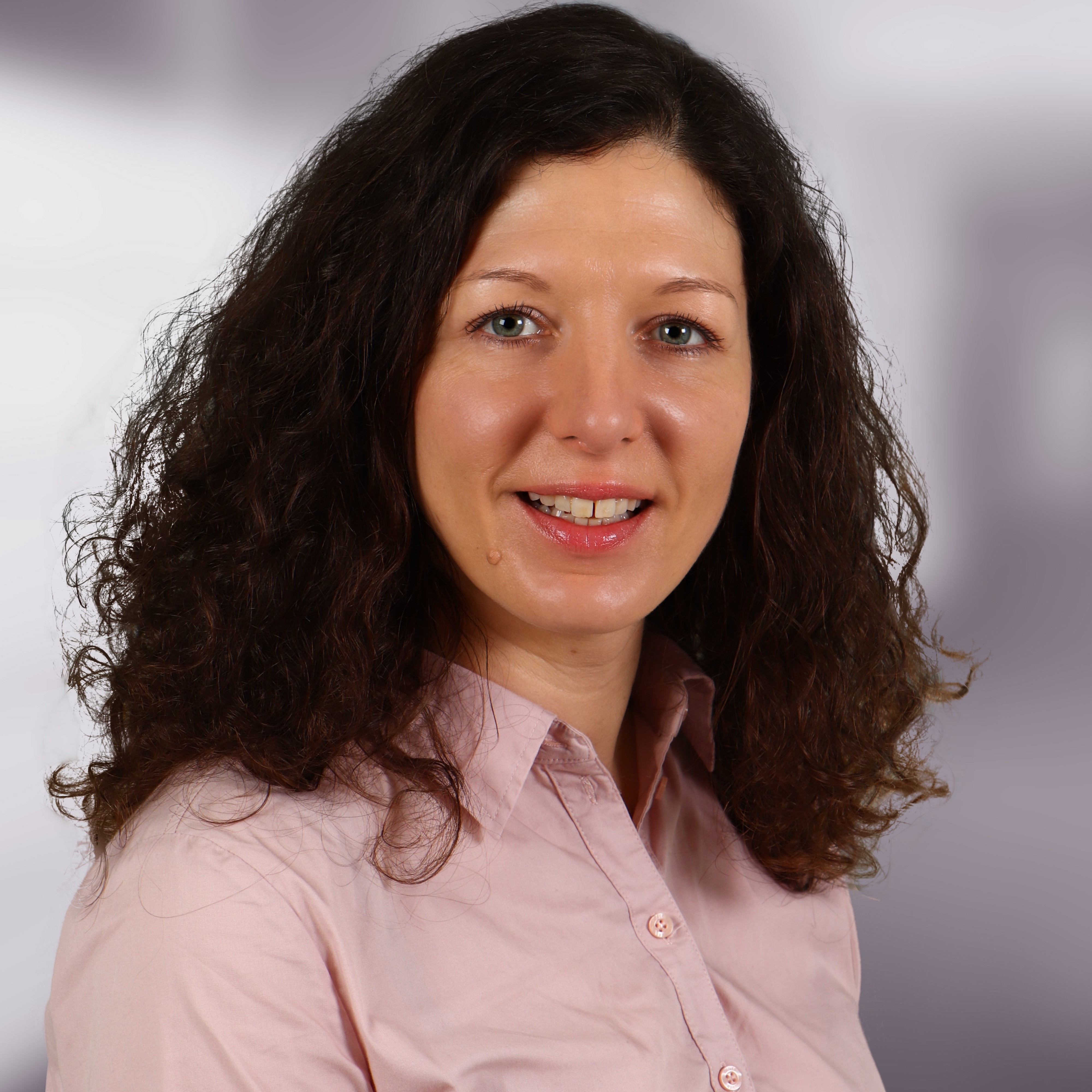 Verhalten am Bahnsteig Anna-Carola Axtmann Das Portrait zeigt eine Frau mit schwarzem, gelocktem Haar in einer rosa Bluse.