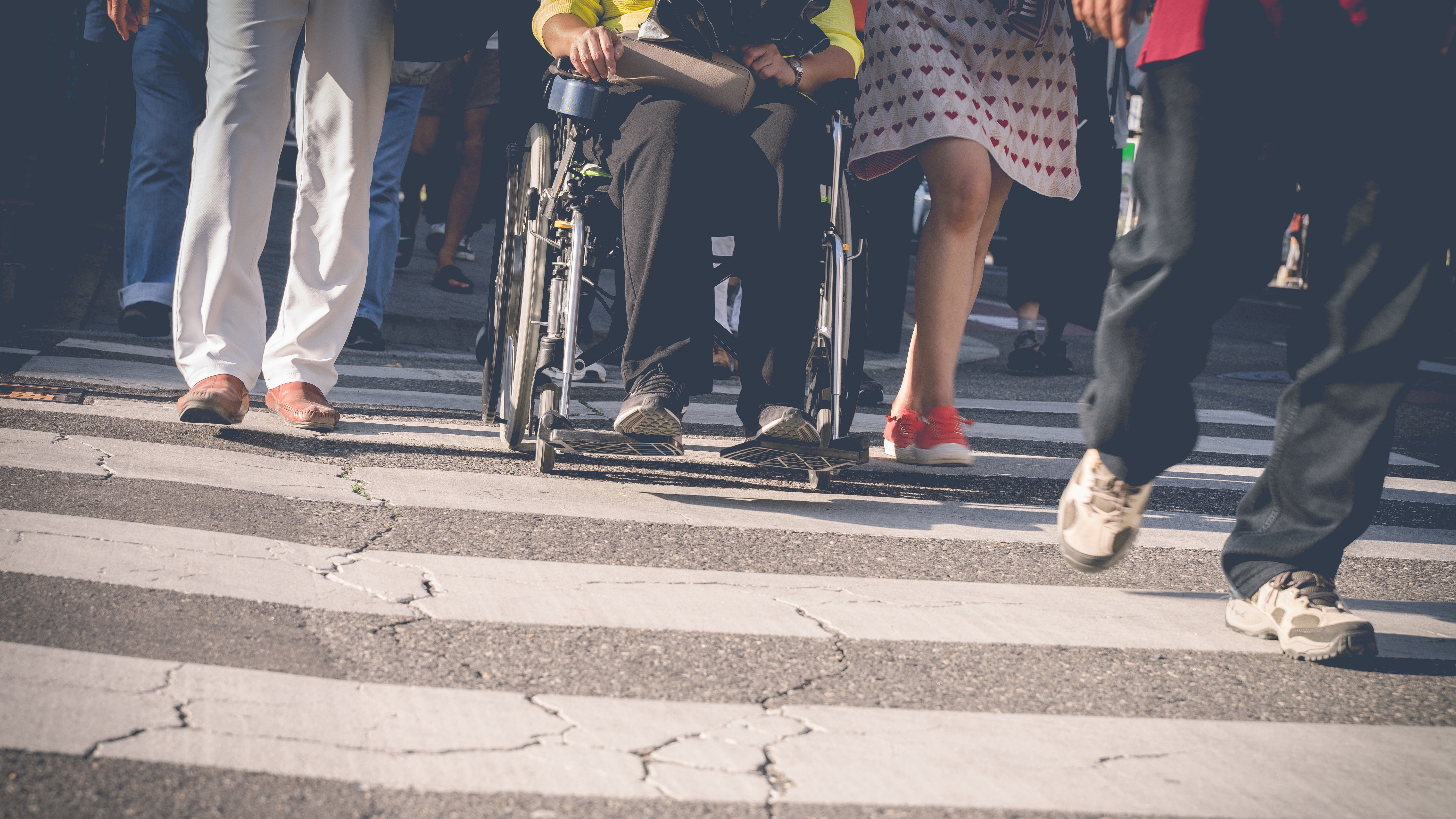 Verkehrssicherheit für Menschen mit Behinderung 16:9 Vier Personen überqueren einen Zebrastreifen, eine Person mit Rollstuhl.