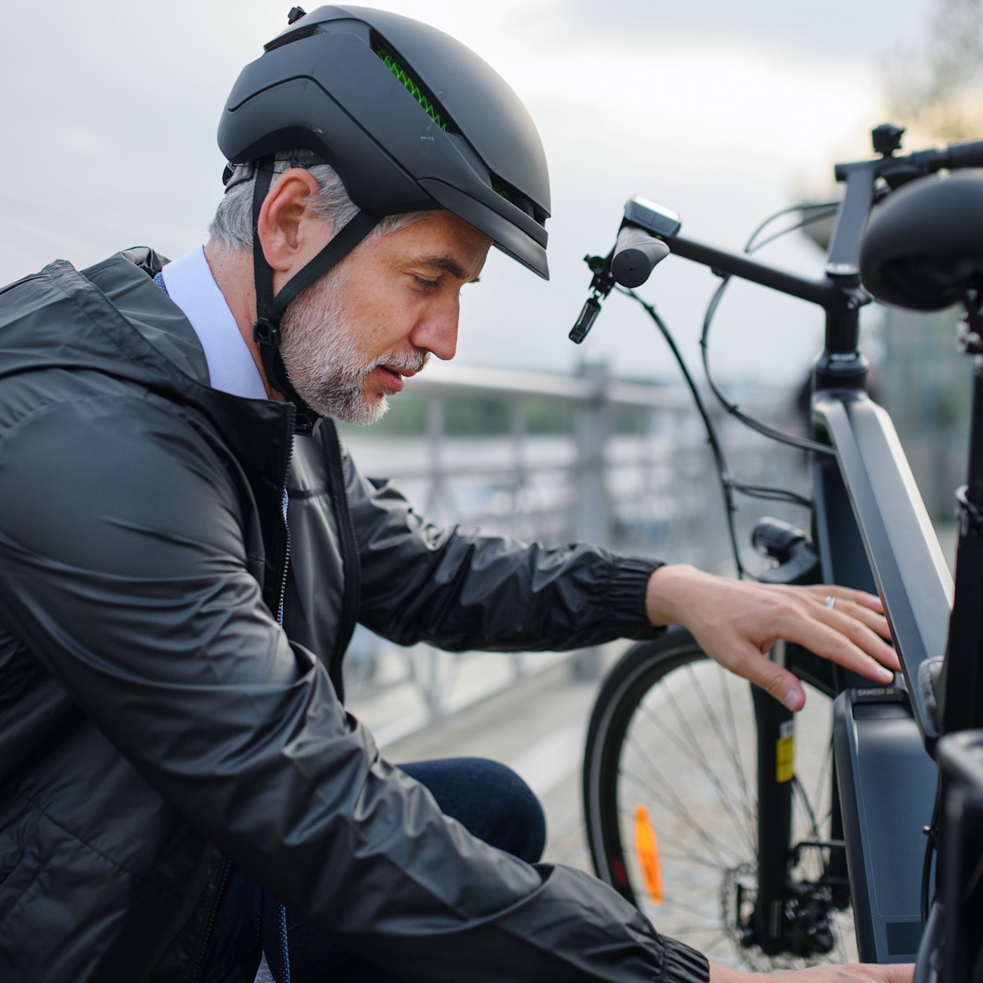 Mann mit Helm vor seinem E-Bike Ein Mann mit Helm kniet vor seinem E-Bike. Im Hintergrund ist eine Brücke zu sehen.