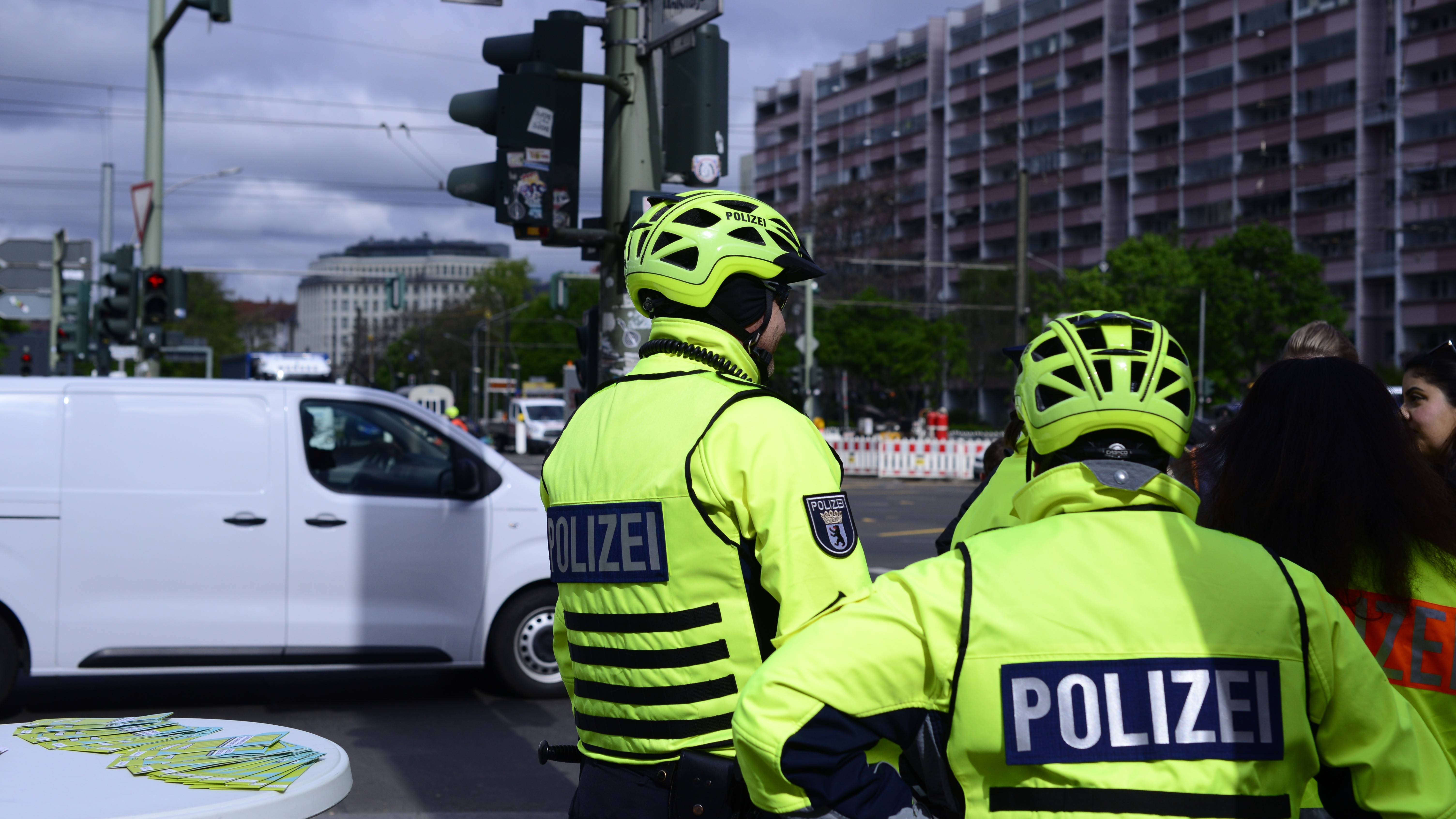 An einer Kreuzung in Berlin sind zwei Fahrradpolizisten von hinten zu sehen. Sie tragen neongelbe Uniformen und Fahrradhelme.