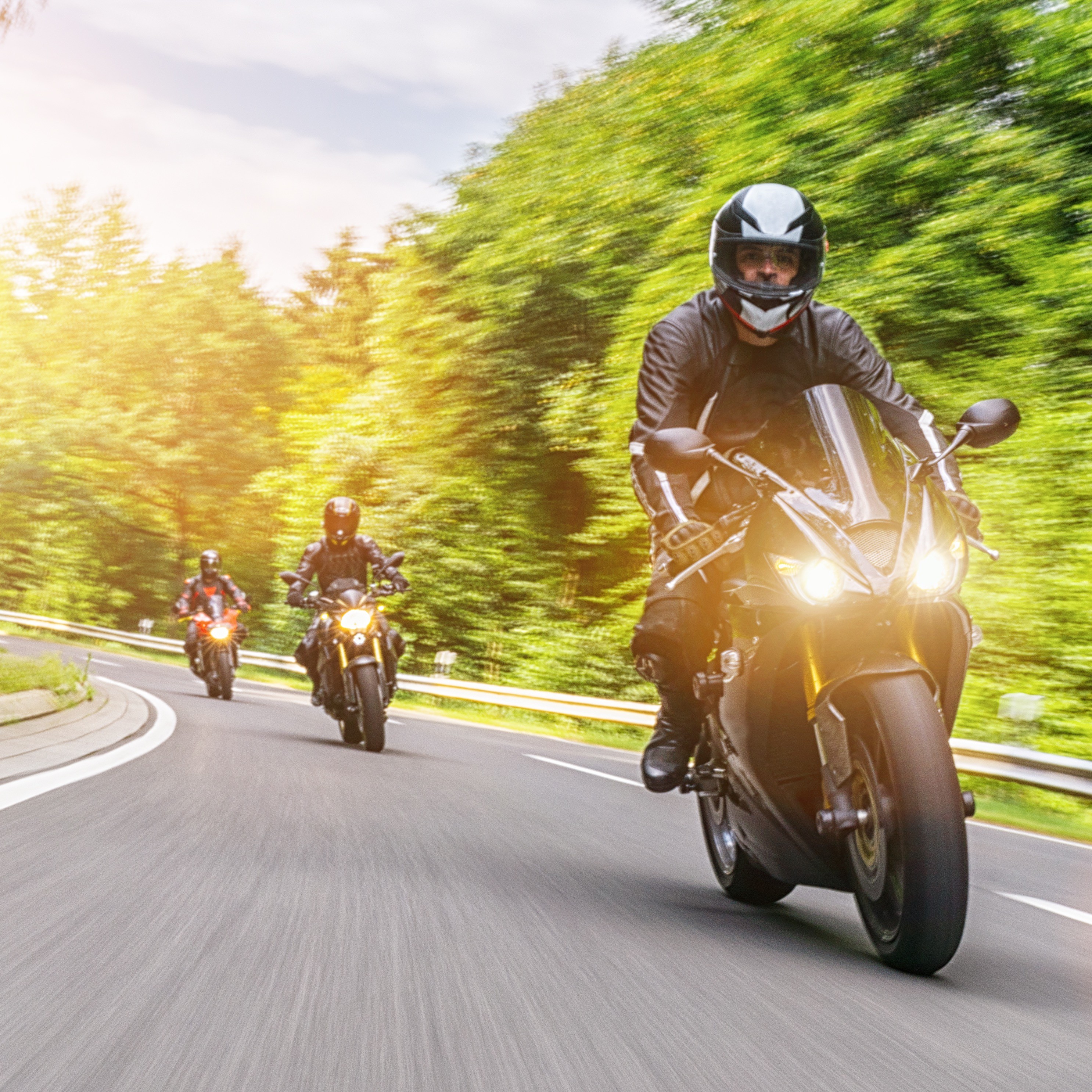 Motorradfahrende in schwarzer Motorradkleidung genießen eine kurvenreiche Landstraße.
