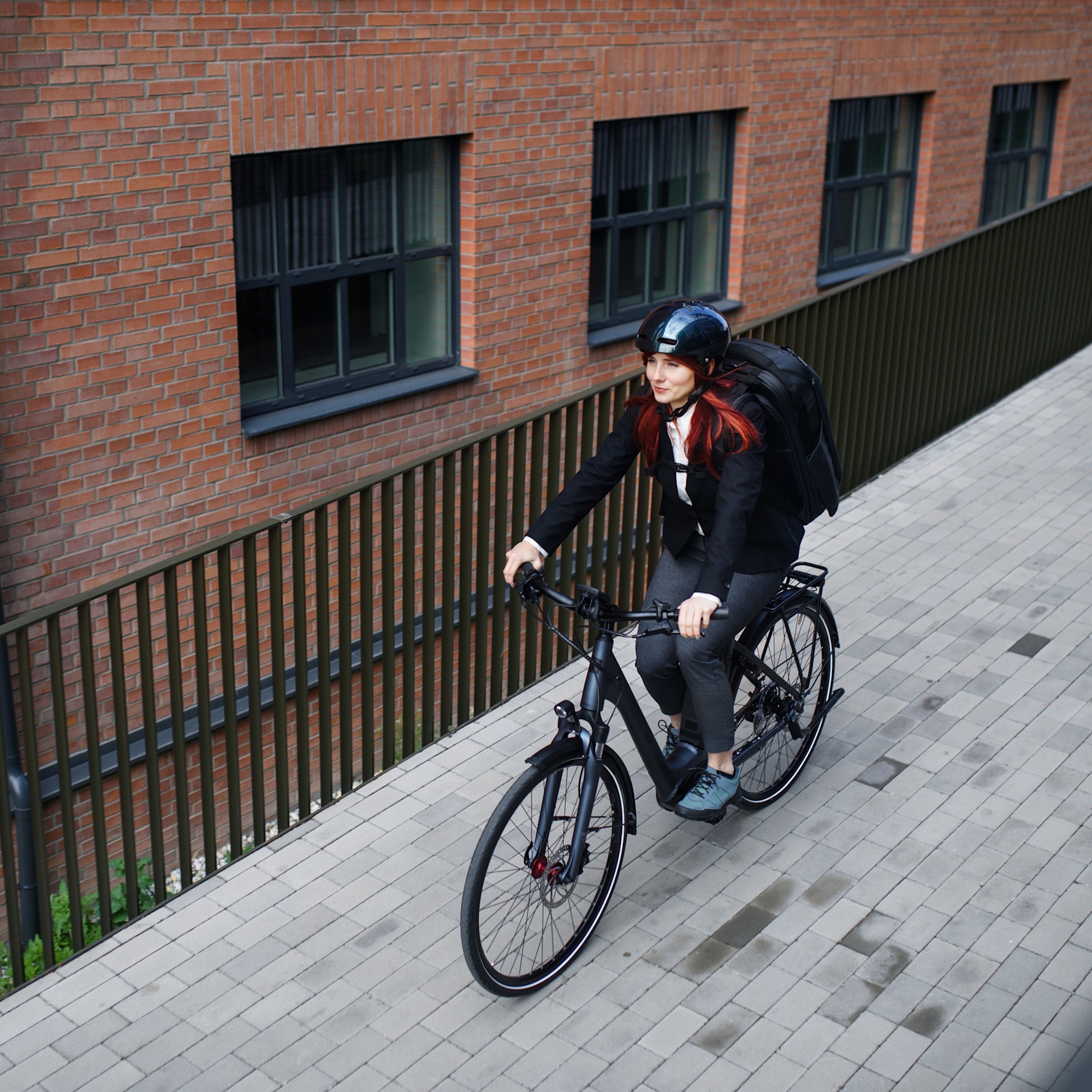 Radsicherheit für Pendelnde Frau fährt Fahrrad 1:1 Eine junge Frau mit Rucksack und Helm fährt mit dem Fahrrad an einer Hausfassade vorbei.