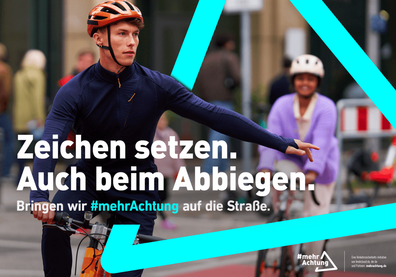 Das Bild zeigt einen Fahrradfahrer mit blauer Jacke und rotem Fahrradhelm. Er hebt die linke Hand und signalisiert so, dass er abbiegen möchte. Hinter ihm fährt eine Fahrradfahrerin in pinkfarbener Jacke und mit weißem Helm. In einem türkisfarbenen Dreieck, das über das Bild gelegt ist und an das Verkehrszeichen „Gefahrenstelle“ erinnert, steht der Text: „Zeichen setzen. Auch beim Abbiegen. Bringen wir mehr Achtung auf die Straße.“