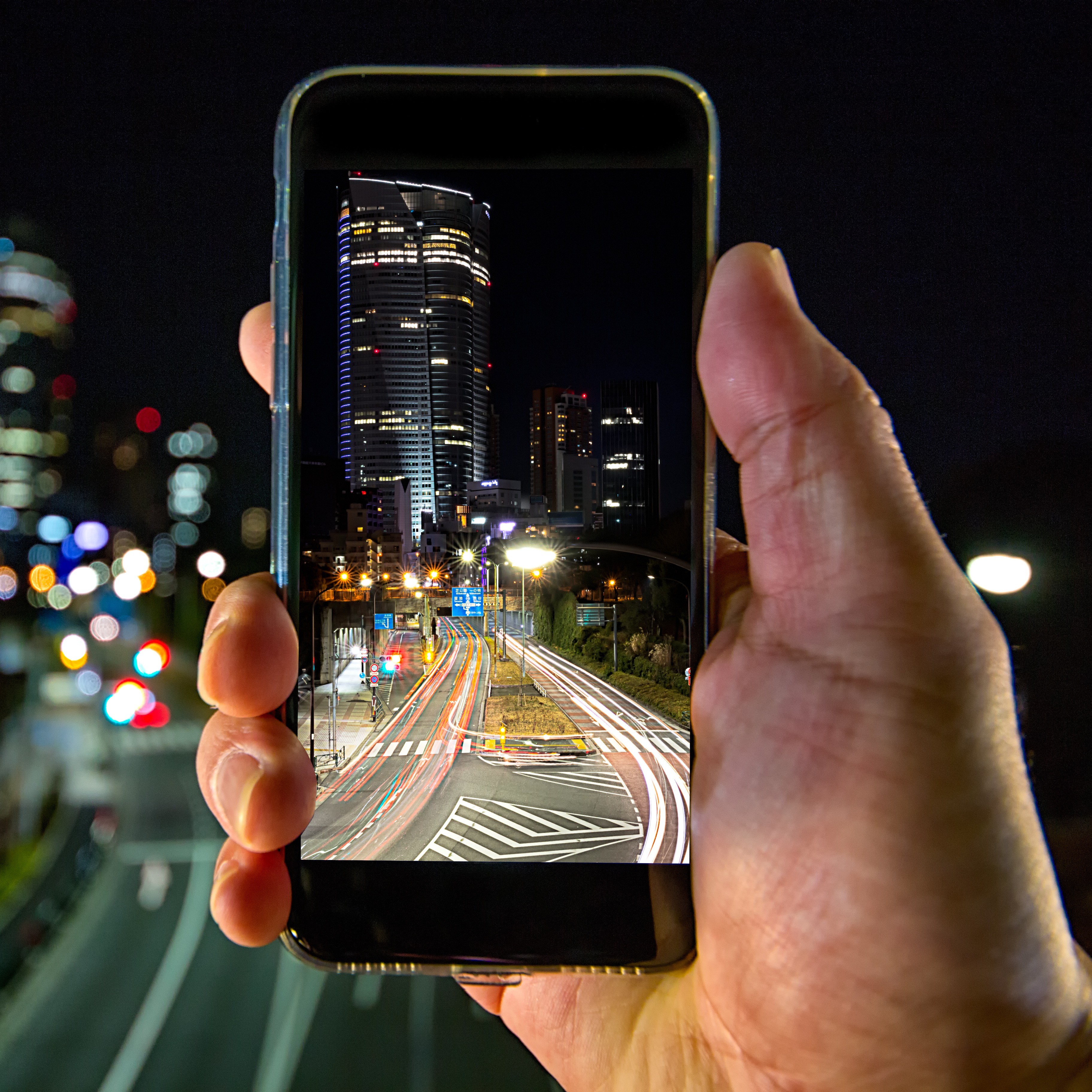 Eine Person hält nachts ein Smartphone, auf dessen Display eine beleuchtete Stadtstraße zu sehen ist.