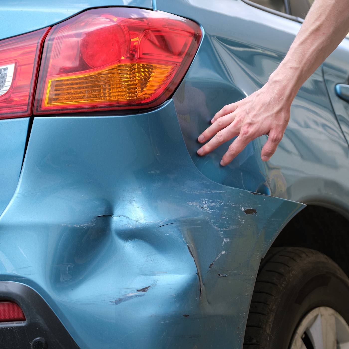 1:1 Mythos oder Wahrheit Eine junge Frau kniet vor einem silberfarbenen Auto und berührt den beschädigten Wagen.