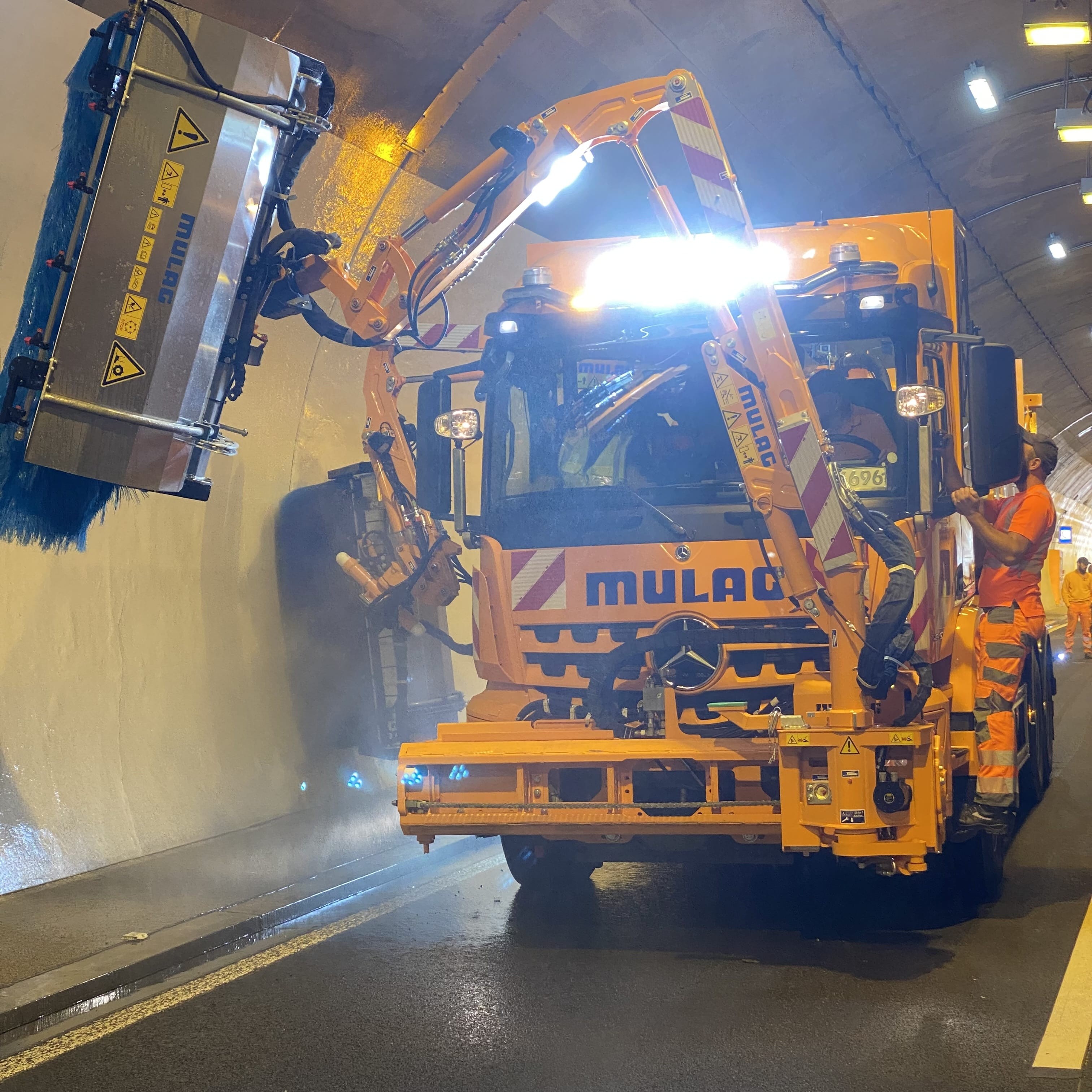 Ein orangefarbenes Waschfahrzeug reinigt eine Tunnelwand.