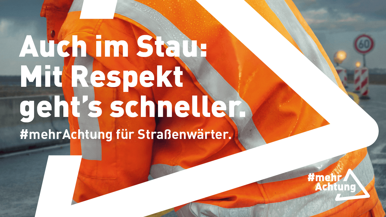 Rückansicht eines Straßenwärters in oranger Warnschutzkleidung bei der Arbeit auf einer nassen Fahrbahn. Im Hintergrund ist eine Baustelle zu erahnen. 