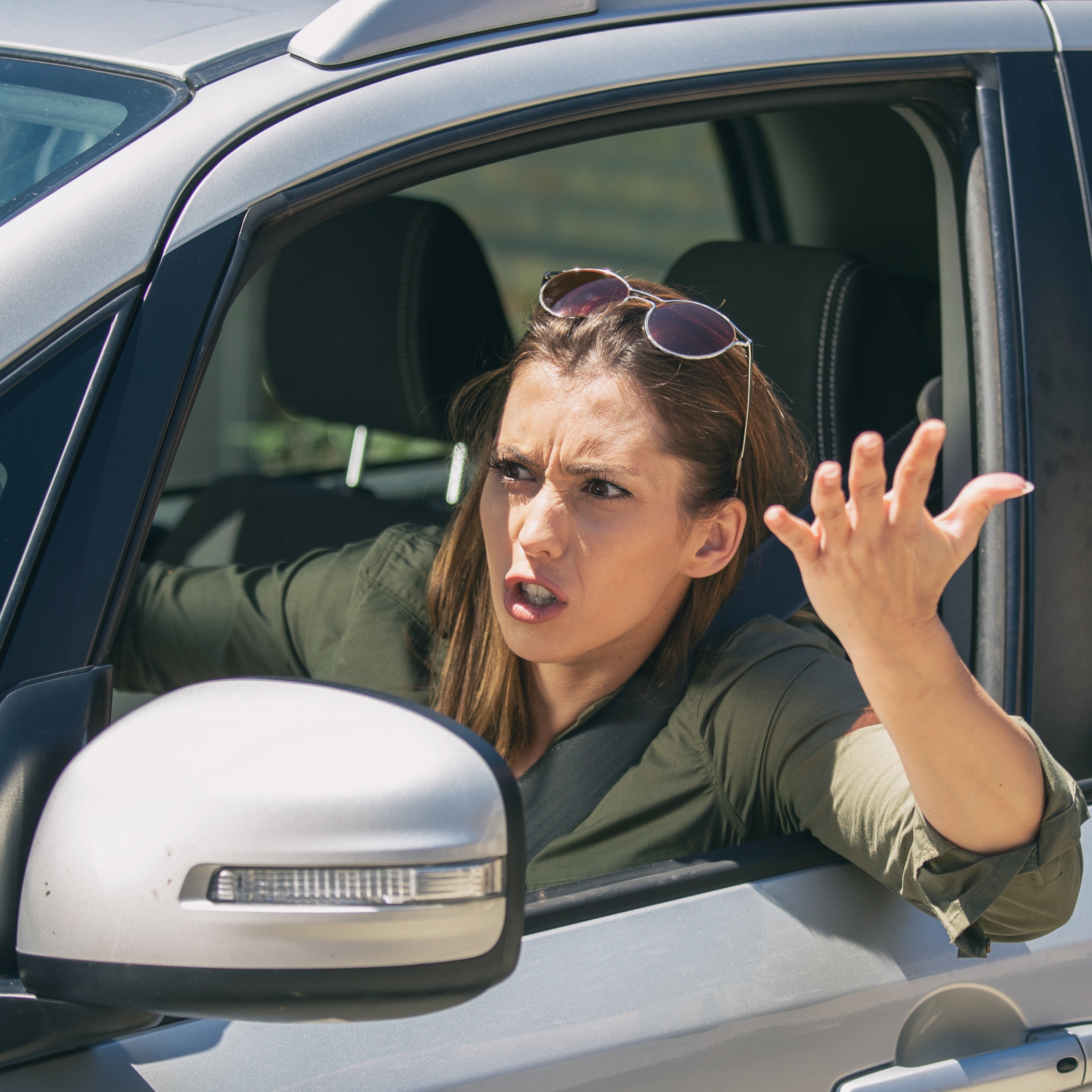 Frau meckert am Steuer Eine Frau sitzt am Steuer eines Autos und gestikuliert aus dem geöffneten Fenster. Sie schaut verärgert.