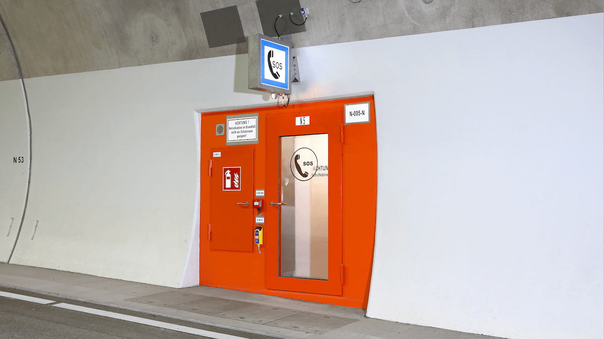 Hinter einer orangefarbenen Tür verbirgt sich eine Notrufkabine in einem Tunnel.