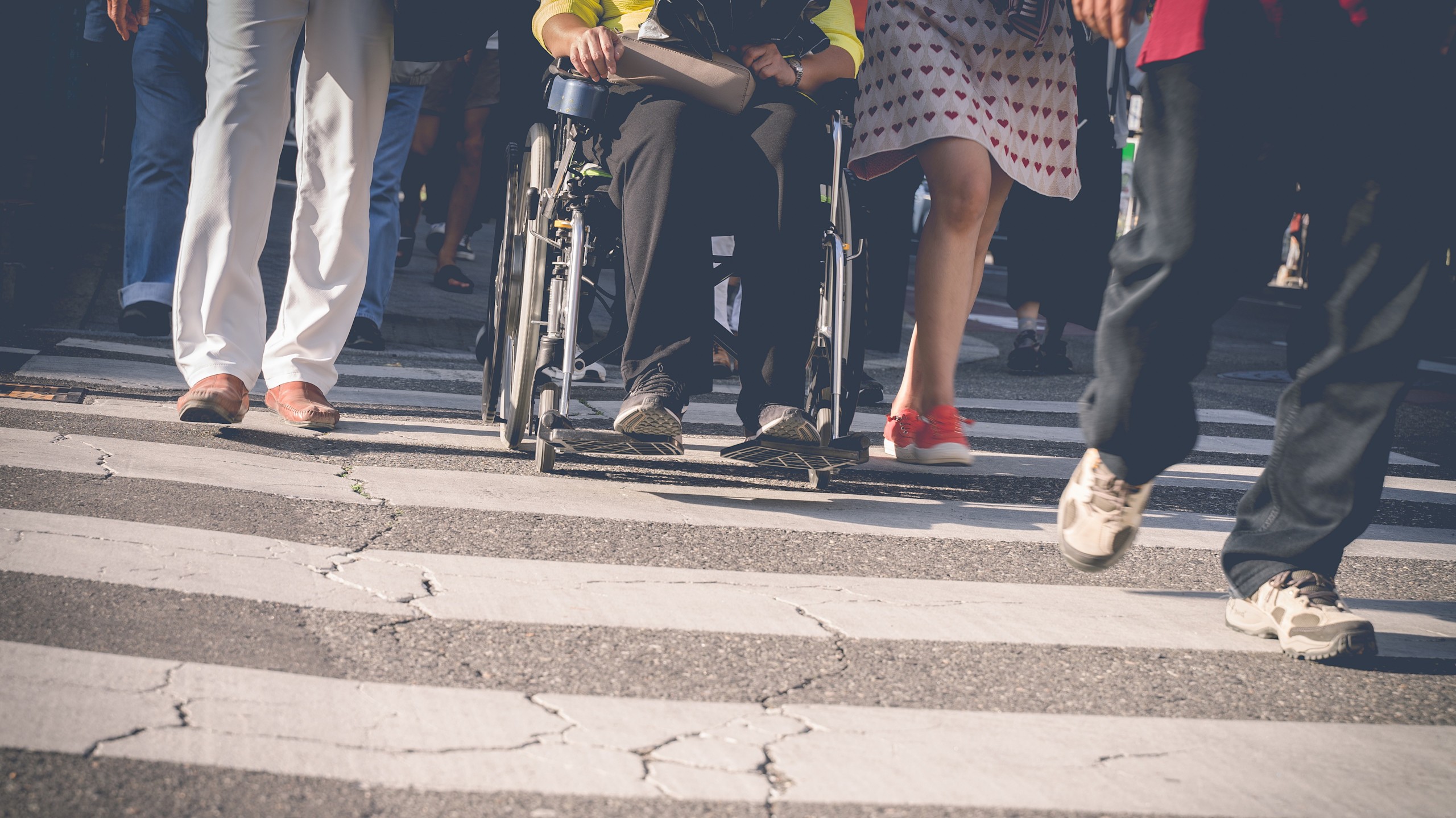 Verkehrssicherheit für Menschen mit Behinderung 16:9 Vier Personen überqueren einen Zebrastreifen, eine Person mit Rollstuhl.
