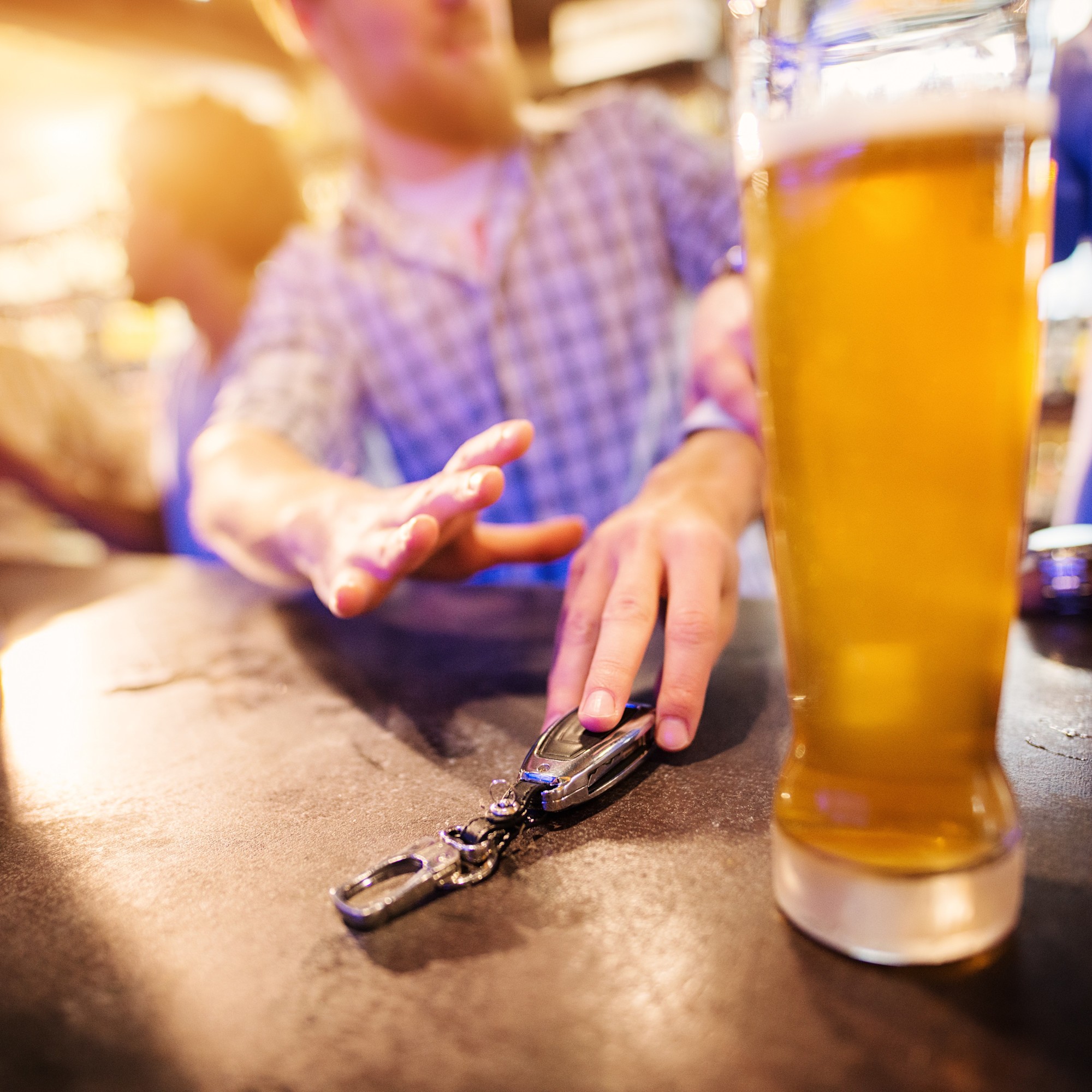 Person greift zum Bier und zu seinem Autoschlüssel 1:1 Zu sehen ist ein Mann in einer Bar, der nach dem Feierabendbier nach seinen Autoschlüsseln greift und dabei zwei Biergläser auf dem Tresen stehen hat.
