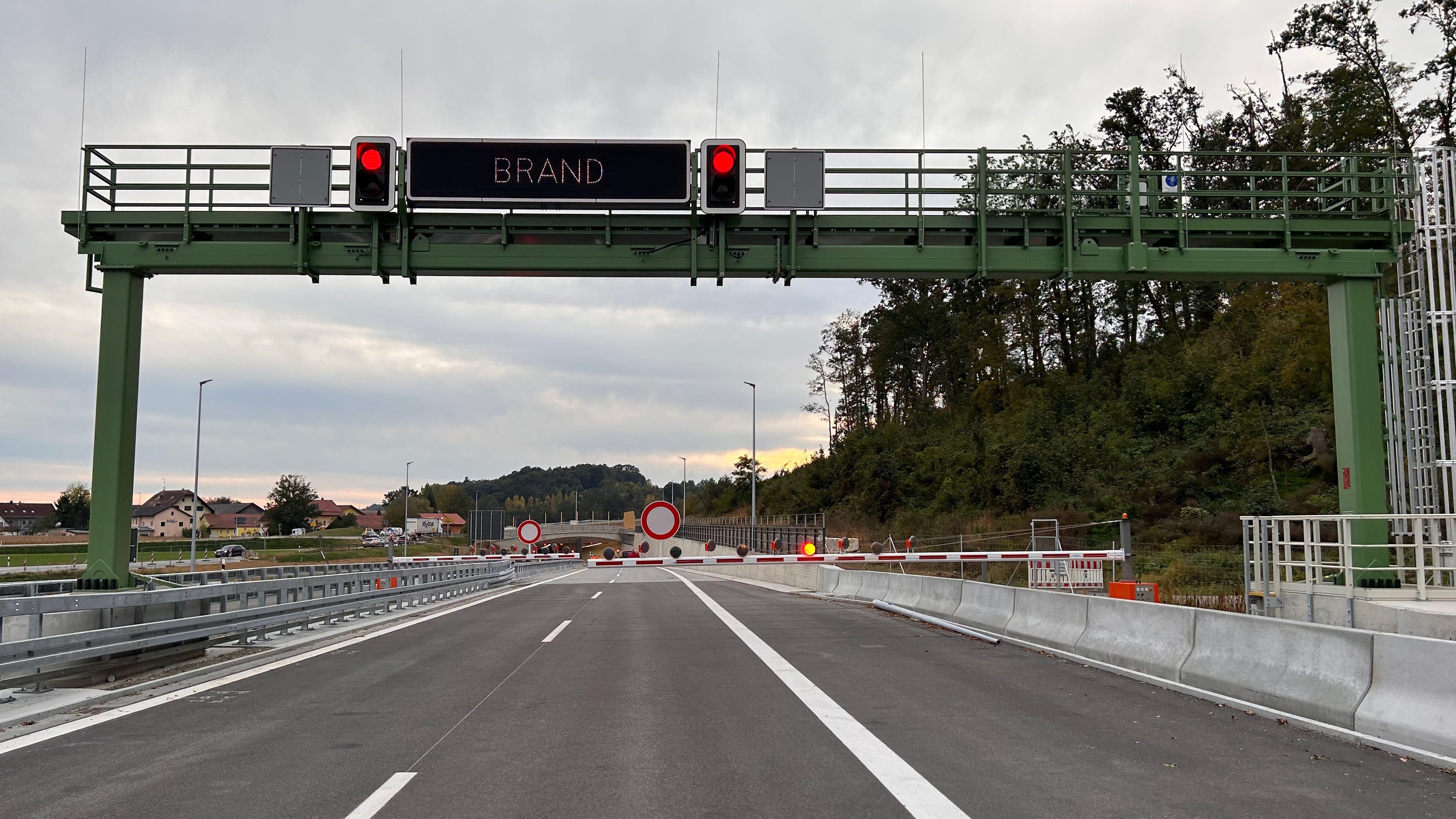 Eine gesperrte Zufahrt zu einem Autobahntunnel. Auf einem Schild steht: „Brand“. Daneben sind rote Ampeln zu sehen. Eine Schranke versperrt die Zufahrt.