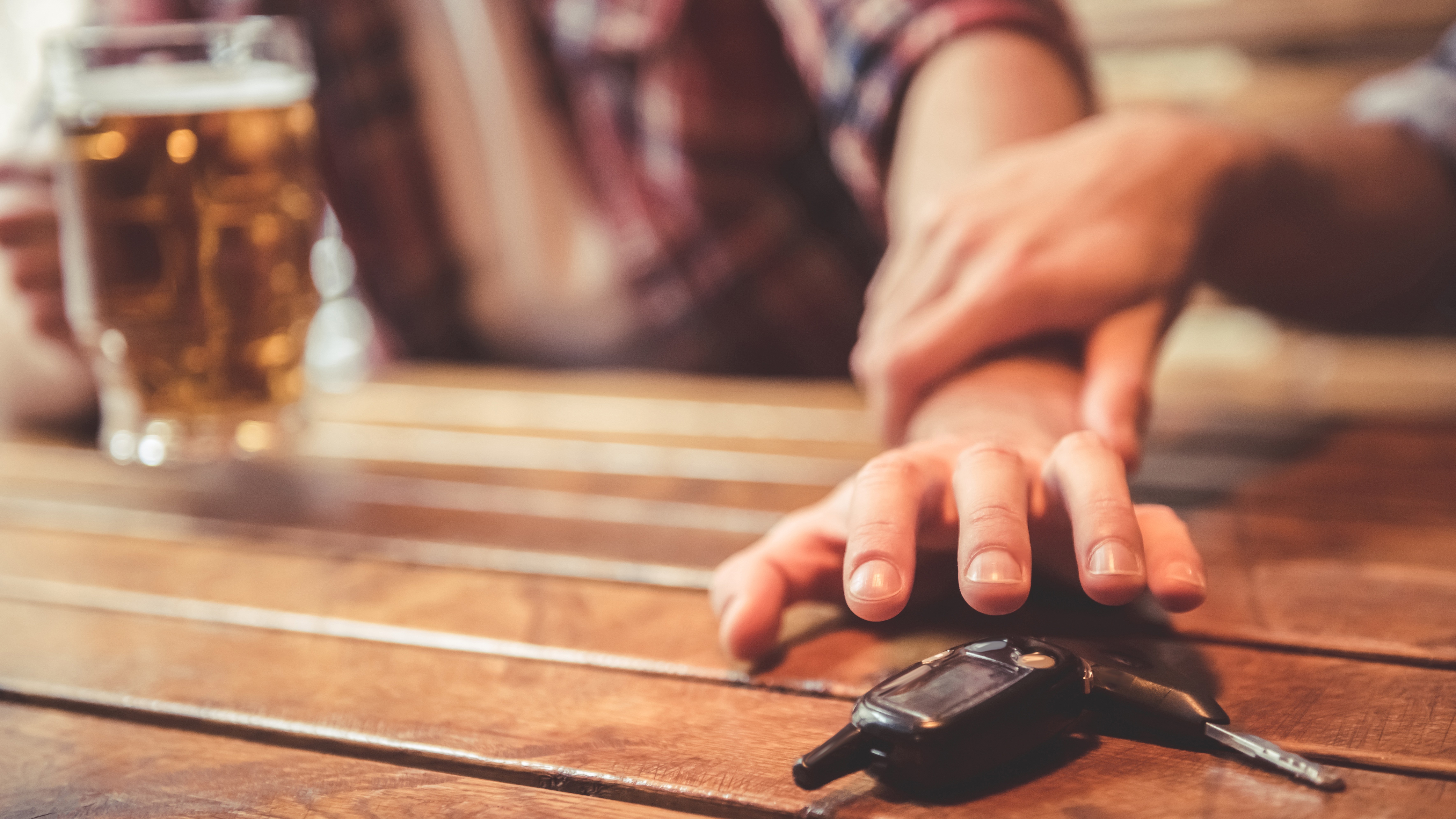 Bild kein Alkohol am Steuer Das Bild zeigt die Hand eines Bier trinkenden Mannes, der nach seinem Autoschlüssel greift. Sein Sitznachbar hält ihn fest, damit er nicht betrunken Auto fährt.
