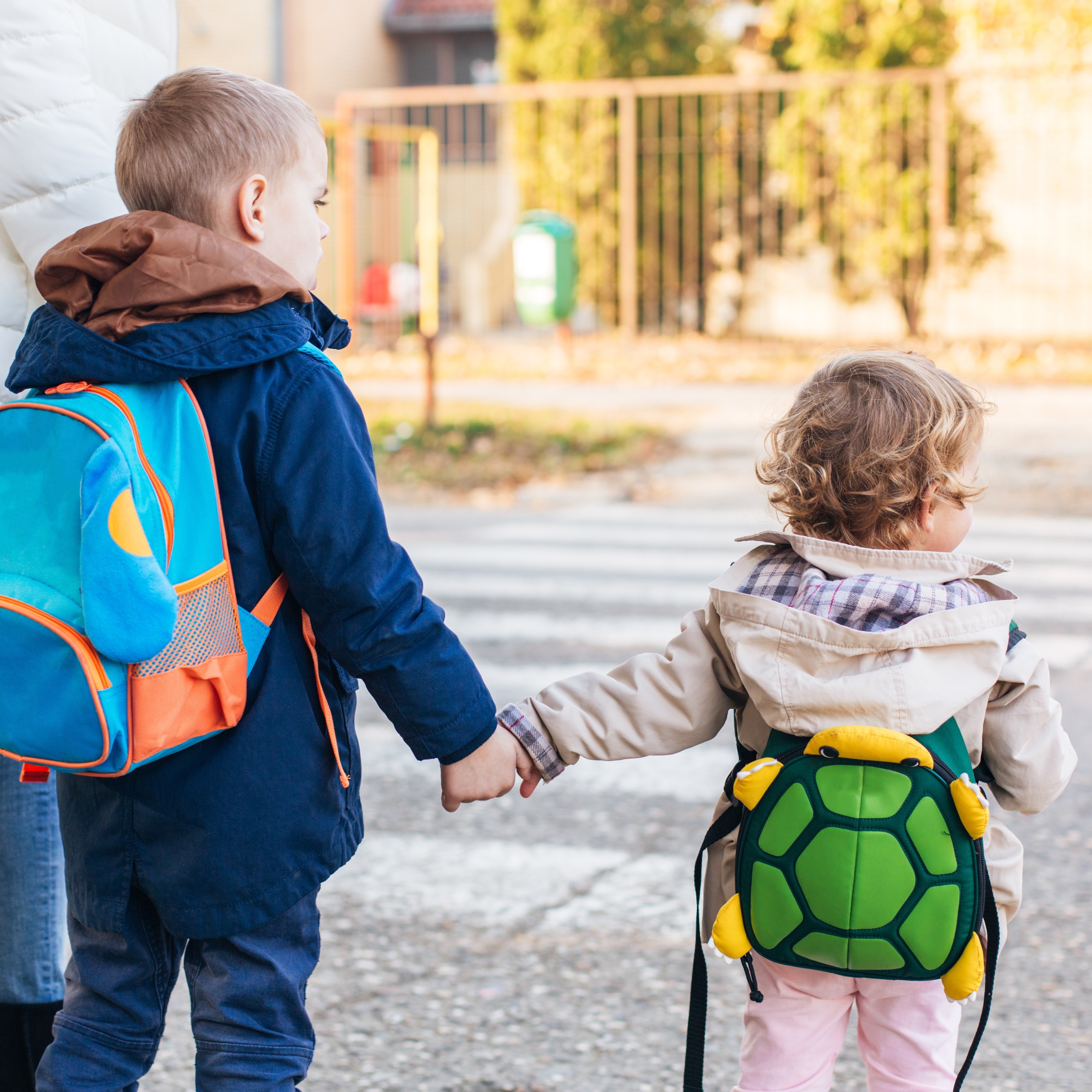 Eine Frau führt einen Jungen im Grundschulalter und ein Kleinkind über einen Zebrastreifen.