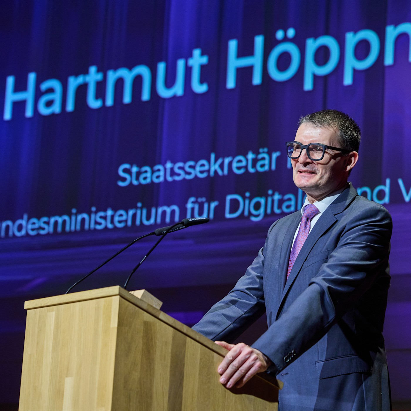 1:1 Hartmut Höppner Ein Mann mit Brille und dunkelblauem Anzug steht an einem Rednerpult. Zu sehen ist Hartmut Höppner vom Bundesministerium für Digitales und Verkehr. Bei der Preisverleihung „Der Rote Ritter“ hält er eine Rede über Verkehrssicherheit.