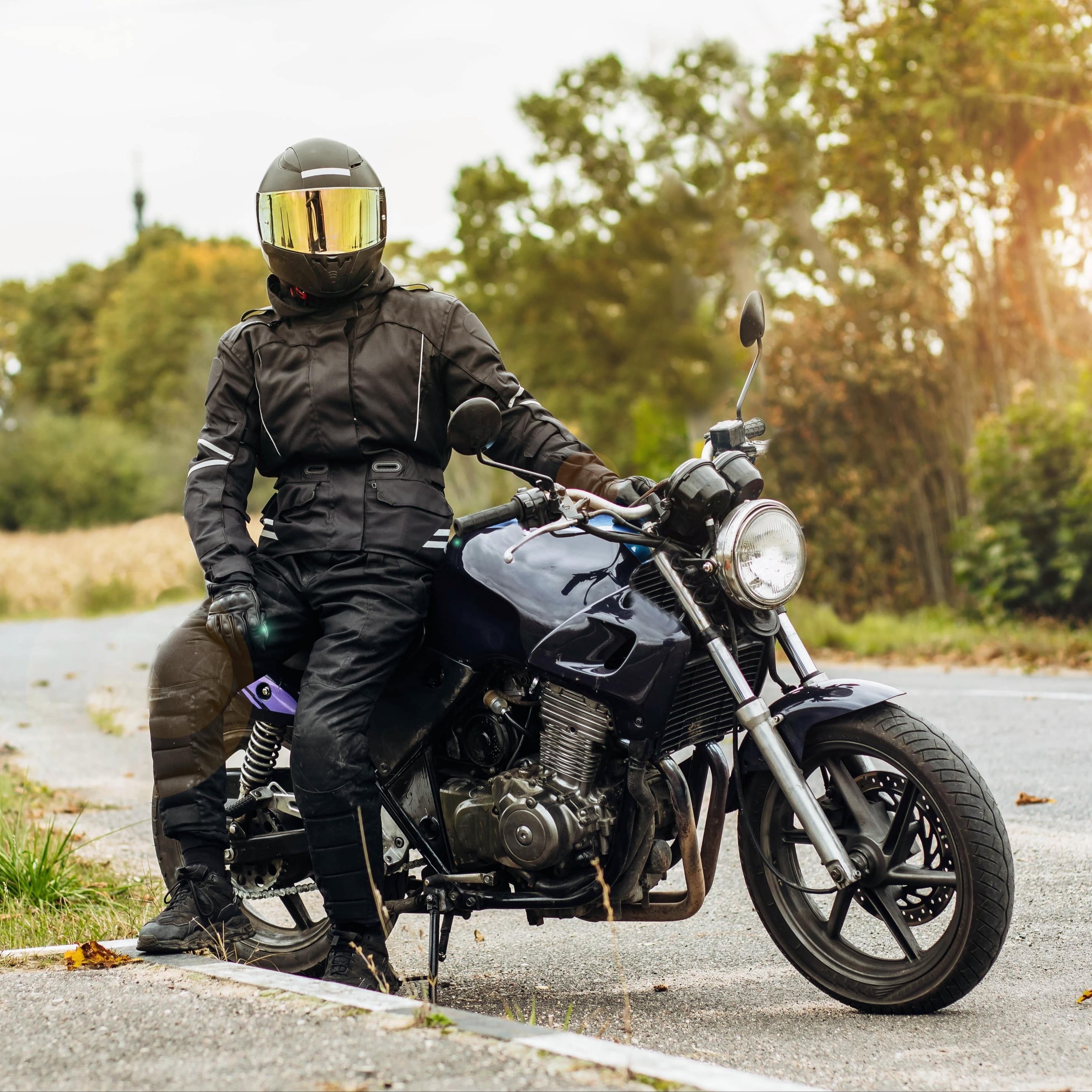 Biker in voller Montur macht eine Pause am Straßenrand. Die richtige Schutzkleidung ist entscheidend für die Sicherheit auf dem Motorrad.